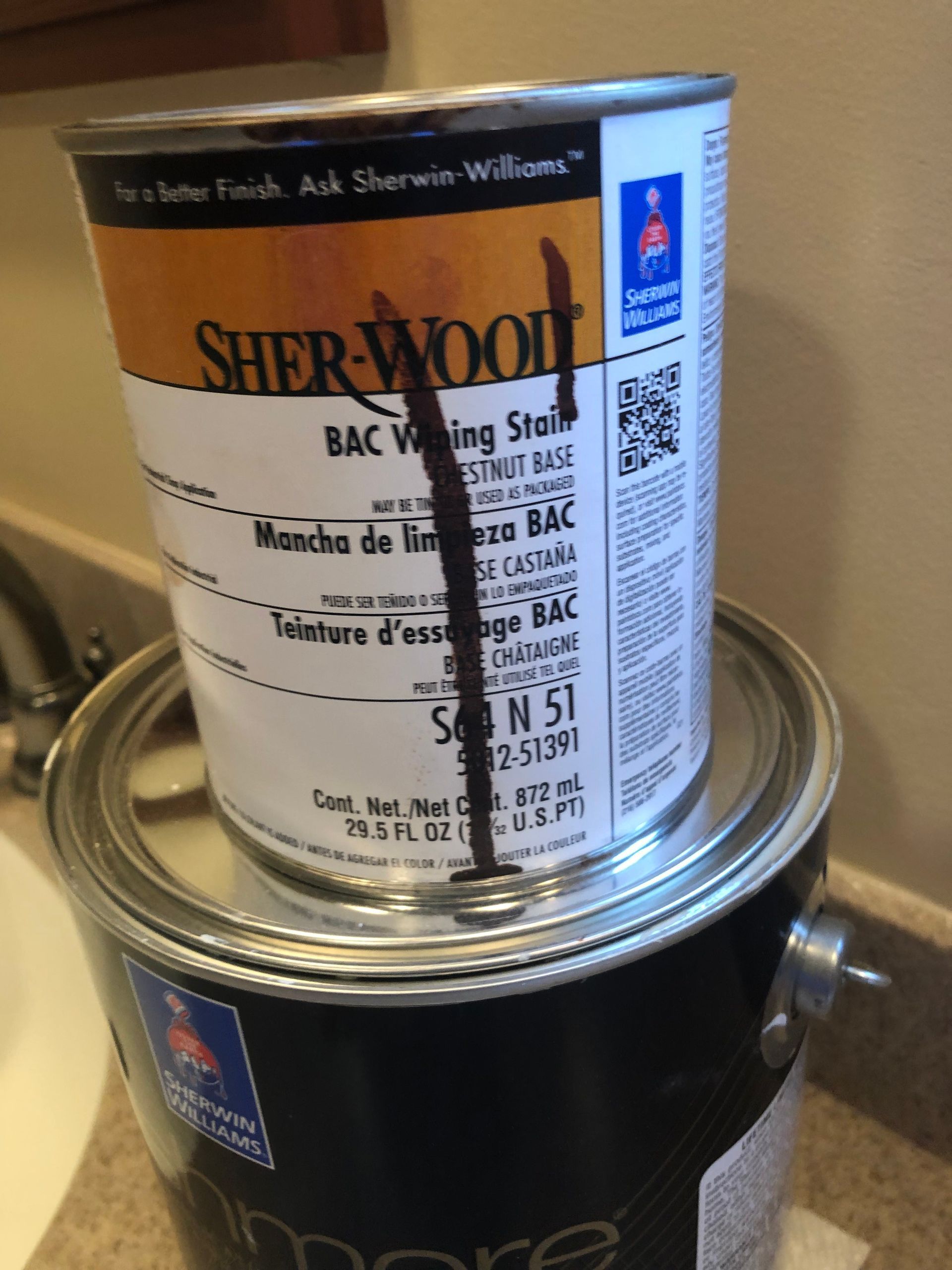 Two paint cans stacked together, one black and one silver, with Sher-Wood labels.