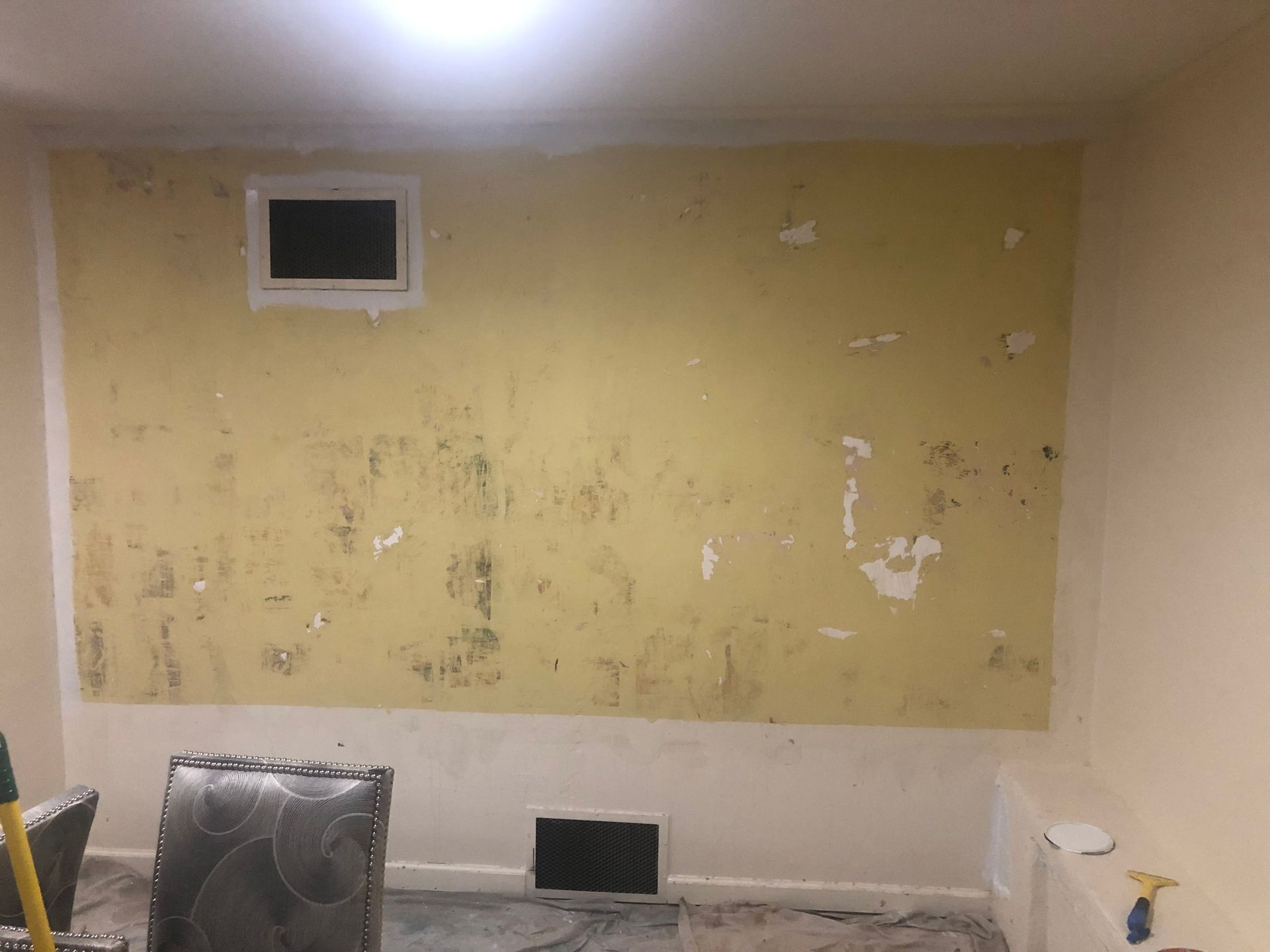 Empty room with yellow wall, damaged peeling paint, and a vent and radiator near the floor.