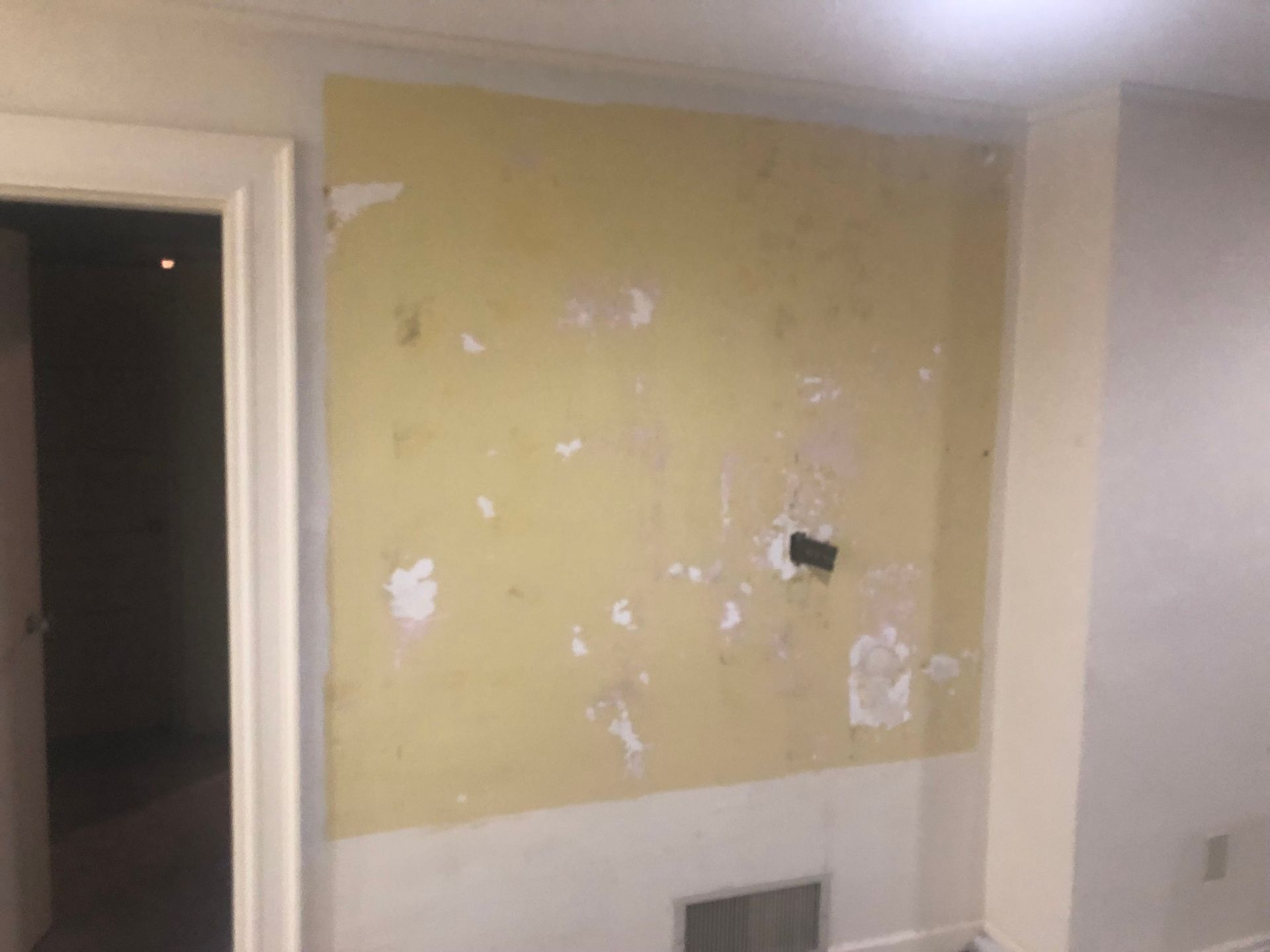 Damaged yellow wall with peeling paint and patch marks in an empty room doorway