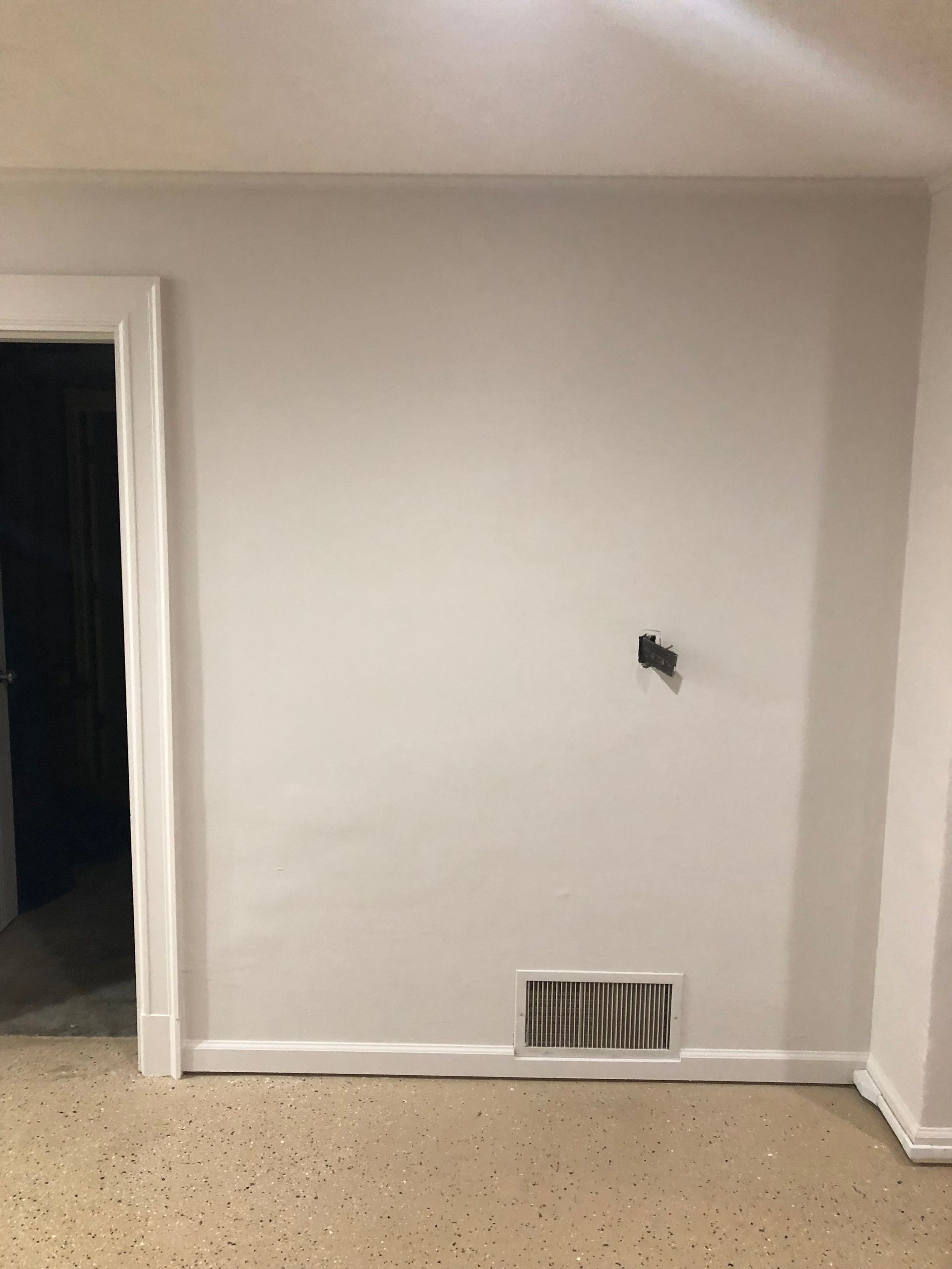 Empty beige interior wall with a vent and a small wall fixture near the center