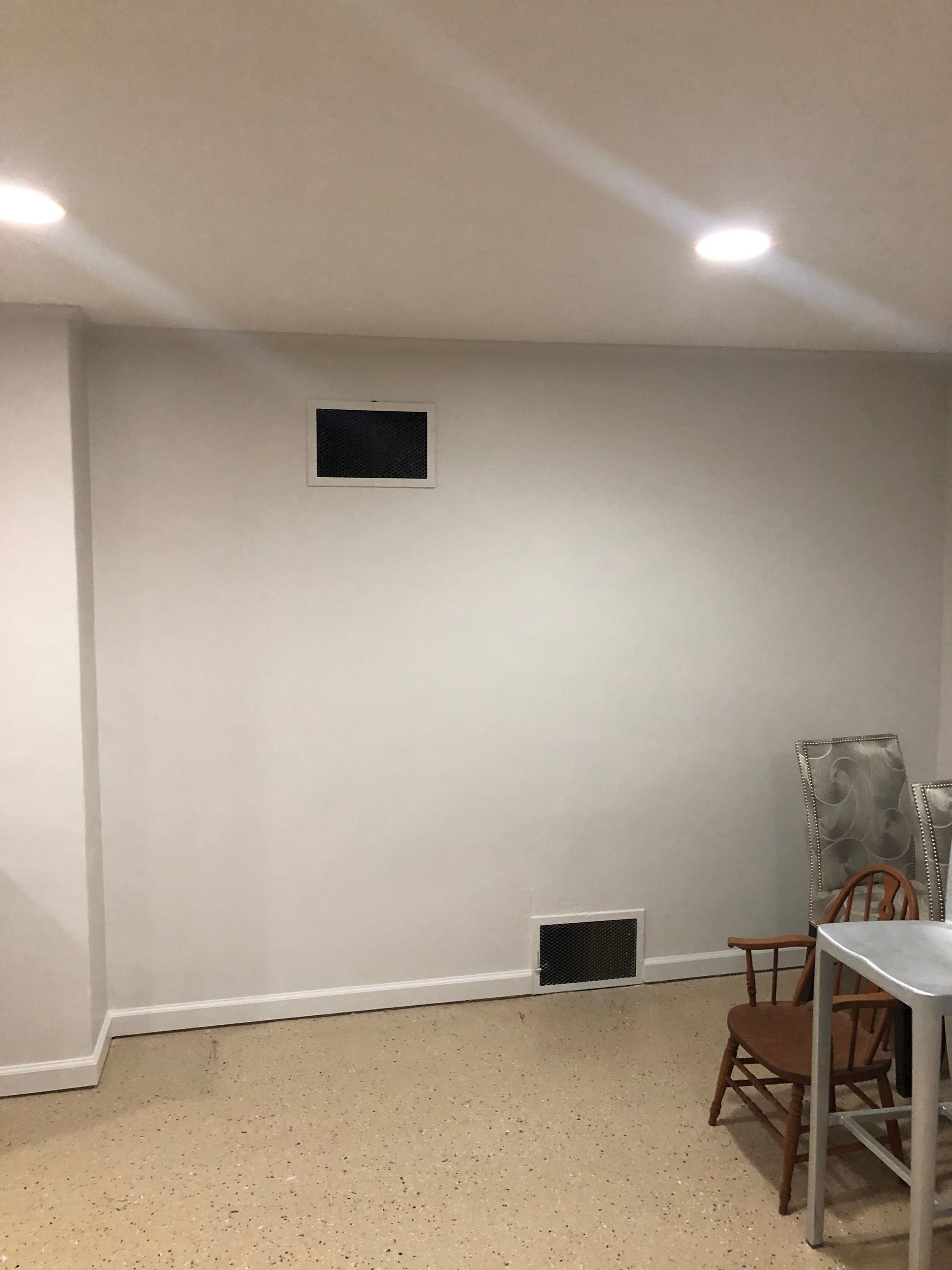 Empty beige room with recessed ceiling lights, small wall vents, and a table and chairs at the right edge