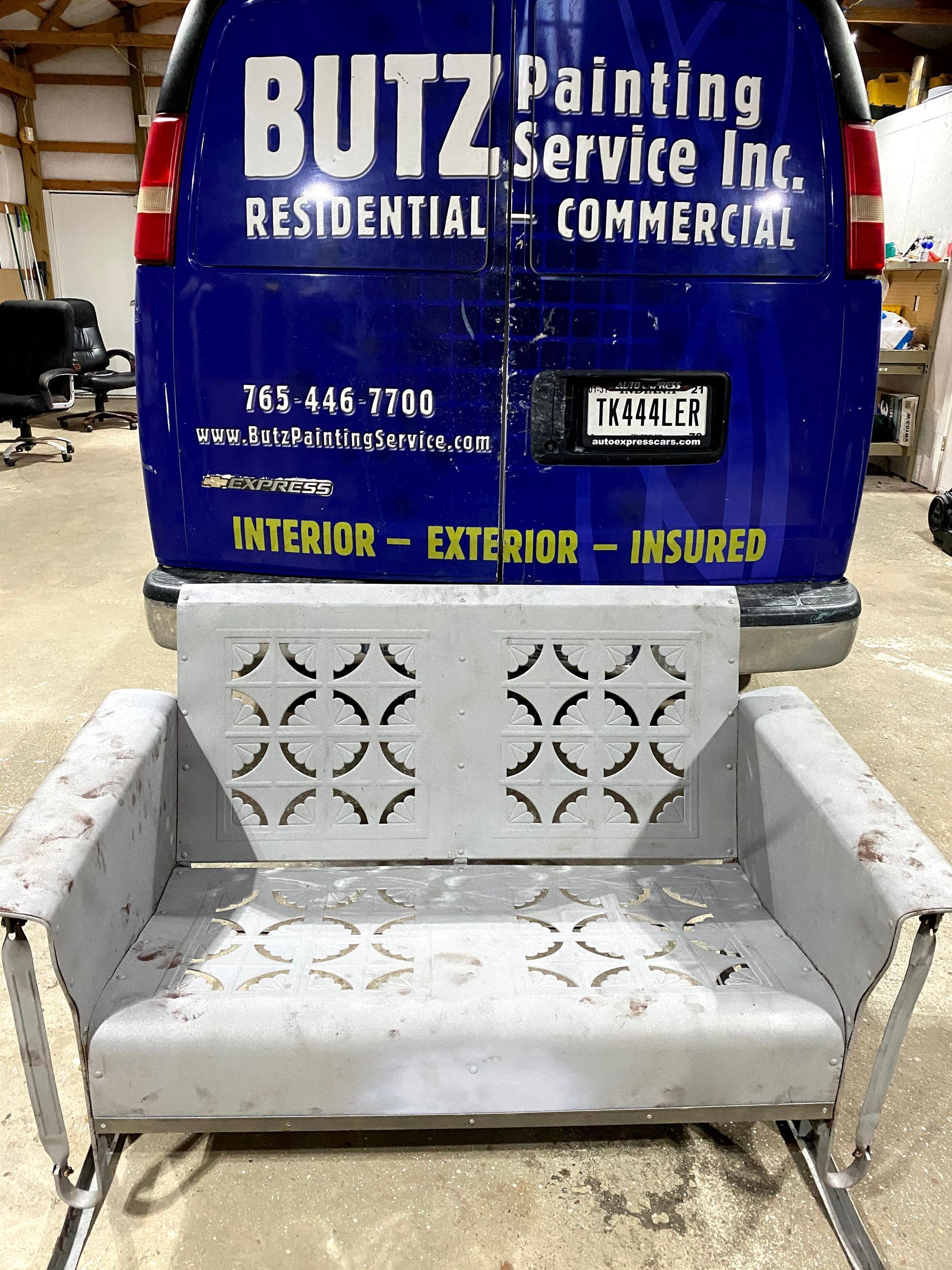 Gray bench in front of a blue Butz Painting Service Inc. commercial sign.