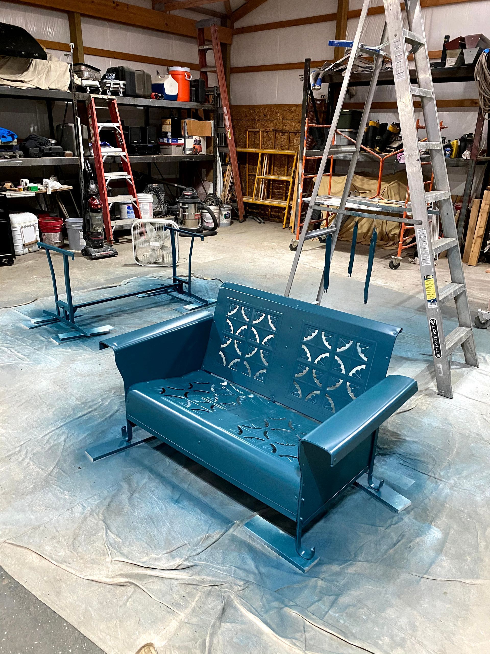 Teal upholstered sofa frames in a garage workshop, with ladders and shelves in the background