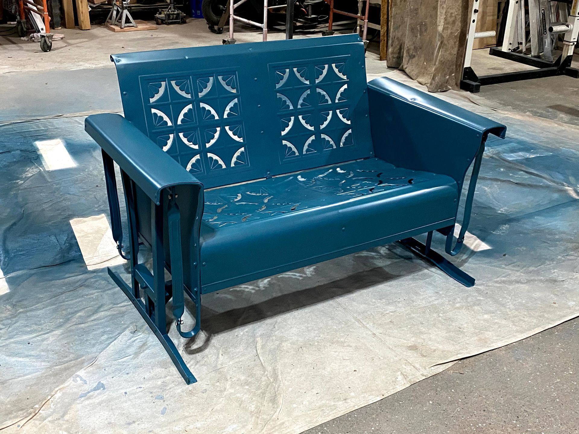 Blue metal bench with decorative backrest on a workshop floor