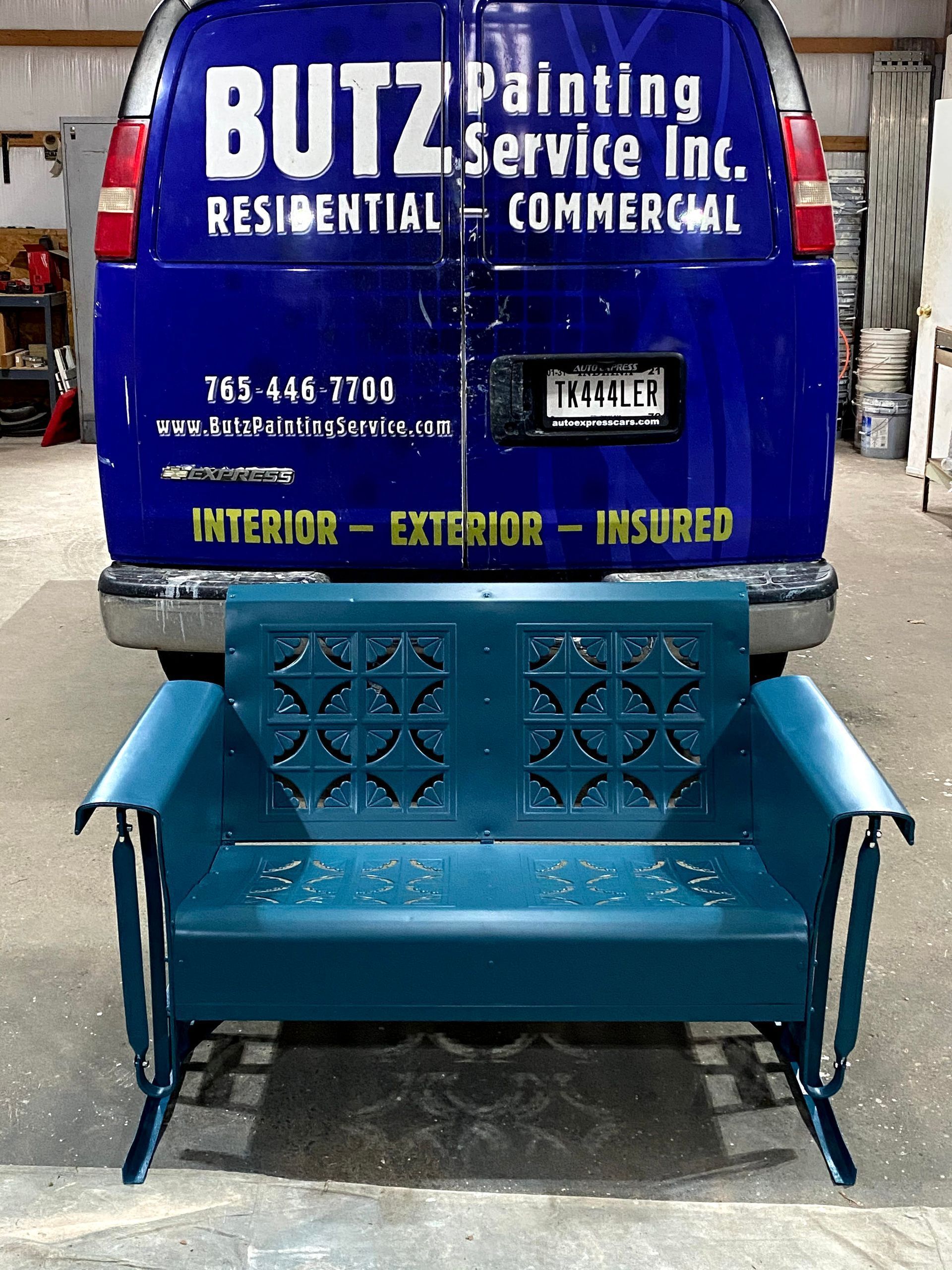 Blue Butz Painting Service van with a teal metal bench attached to the rear, parked indoors