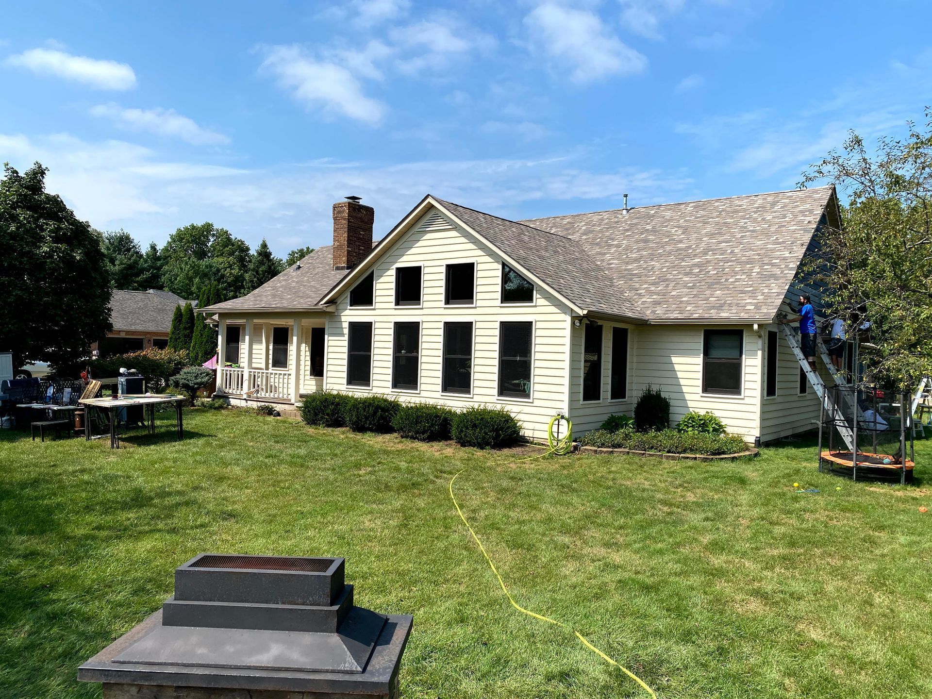 Cream-colored house with black shutters, brick chimney, and a large grassy yard under a blue sky