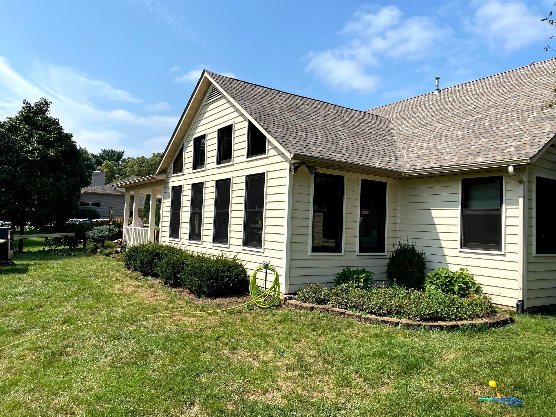 White house with dark shutters and a steep roof beside a grassy lawn under a blue sky