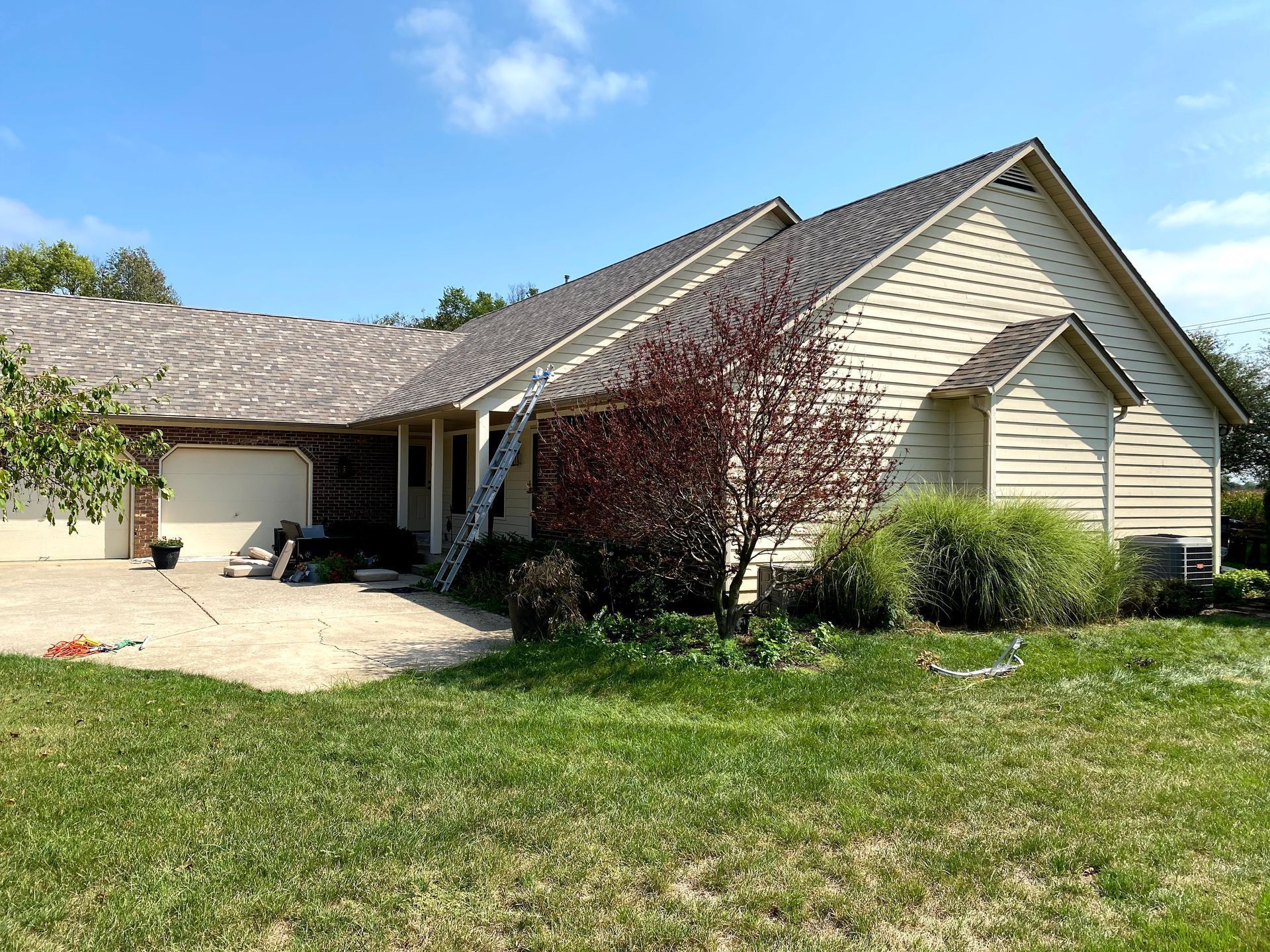 Single-story beige house with a gray roof, front lawn, and attached carport under a clear blue sky