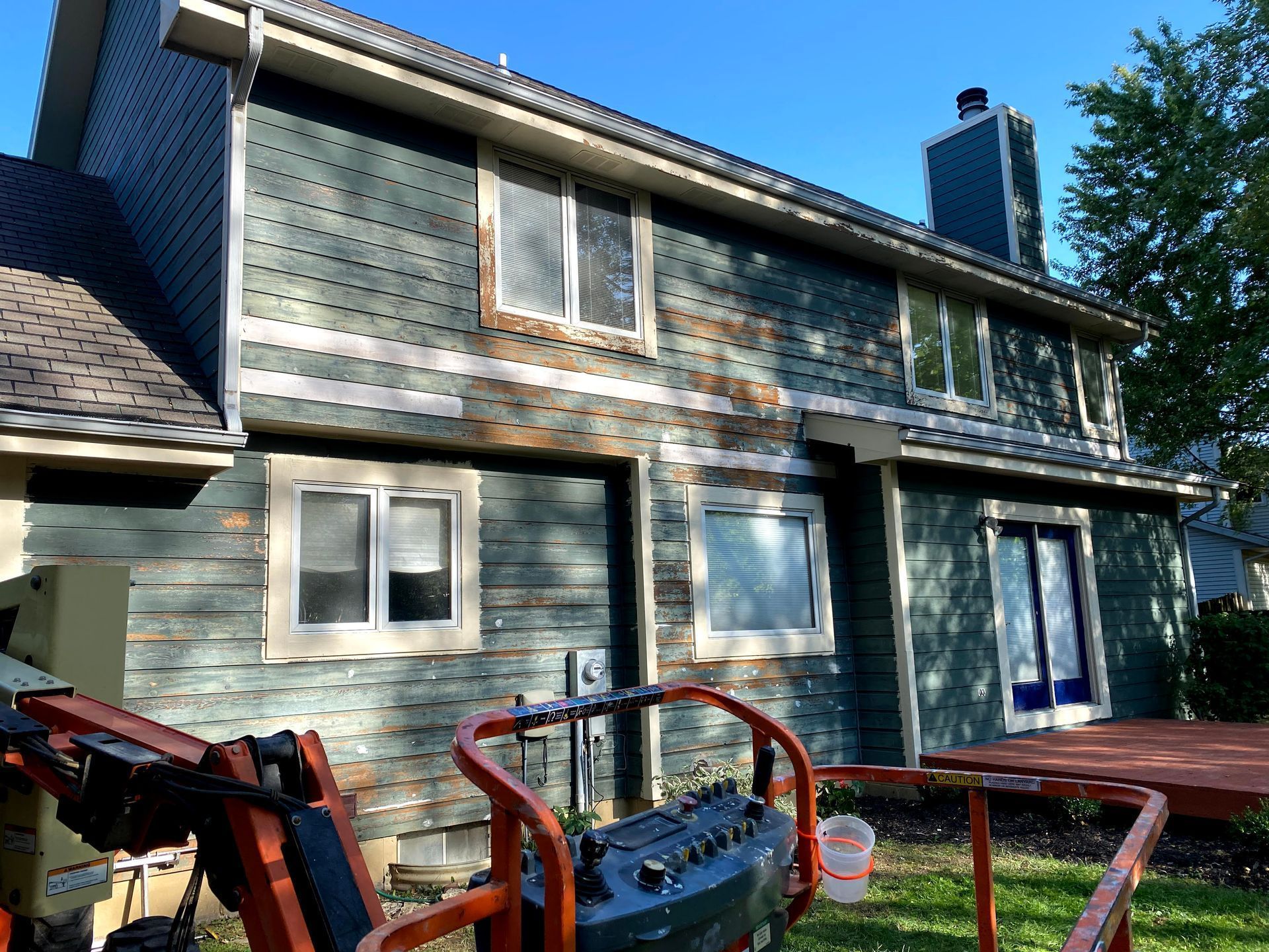 Two-story blue house under renovation with red scaffolding and construction equipment in front