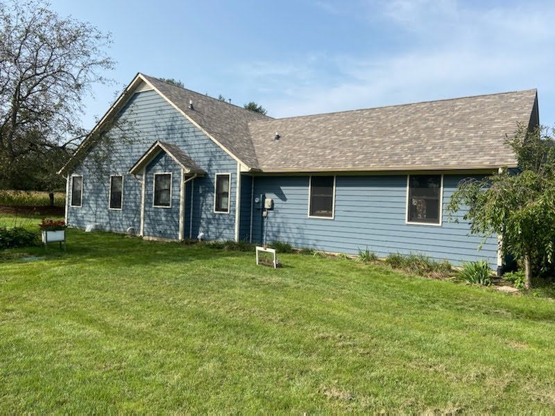 Light blue house with gray roof and front gable, set beside a green lawn under a clear sky