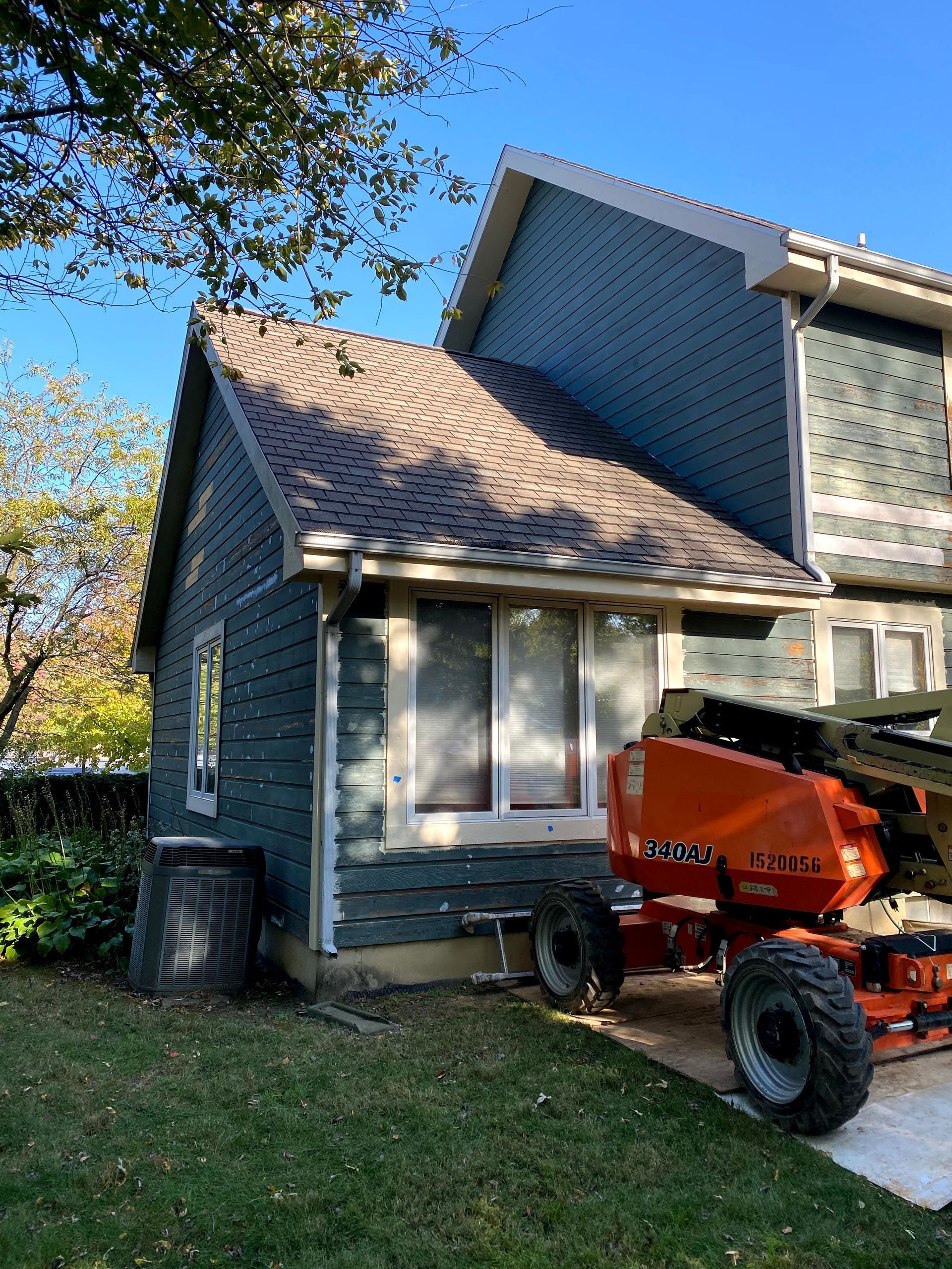 Two-story house with gray siding and tan roof, partially obscured by an orange lift in the driveway.