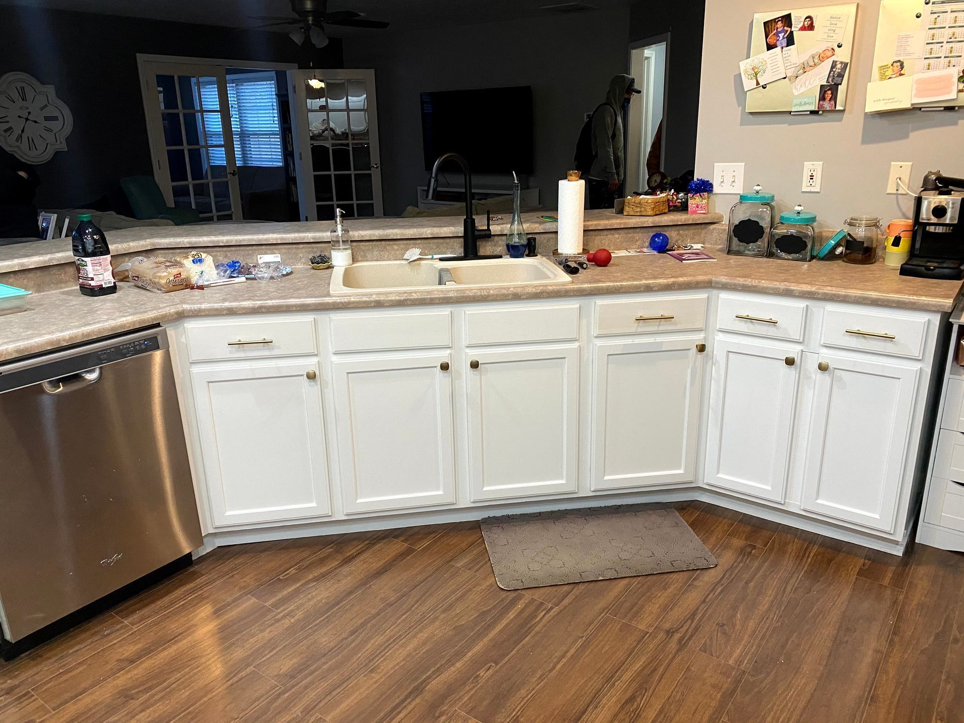 Cluttered kitchen with white cabinets, stainless dishwasher, and scattered items on the countertop.