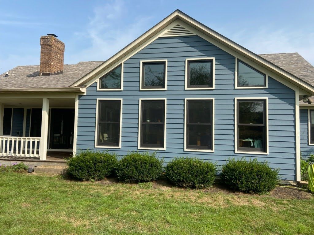 Blue house exterior with white-trimmed windows, gray roof, brick chimney, and front porch in a grassy yard