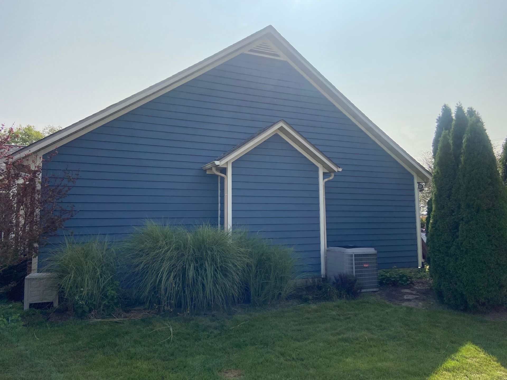 Blue house exterior with white trim, front shrubs, and a grassy yard under a clear sky