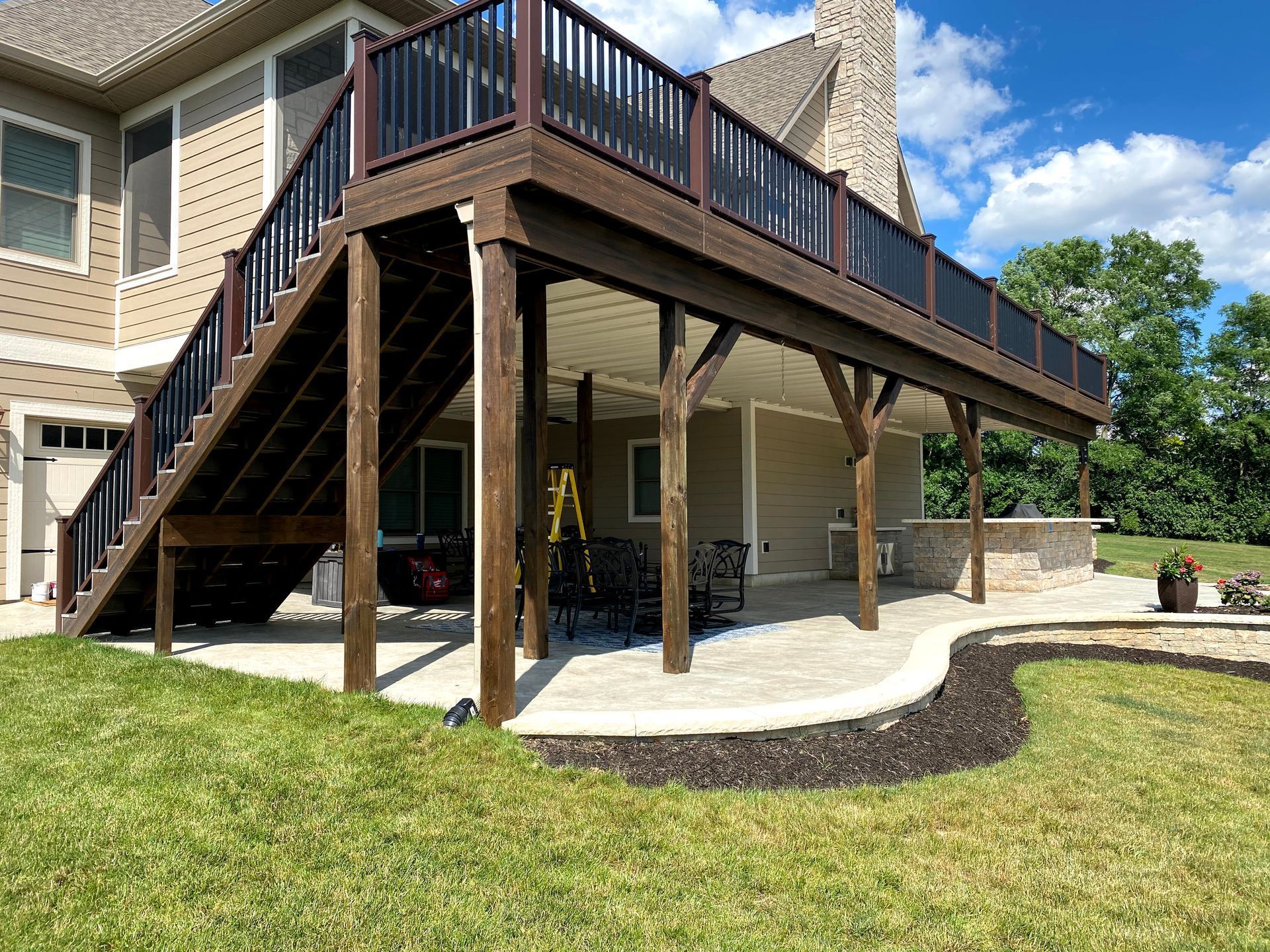 Raised wooden deck with stairs and support posts beside a beige house over a concrete patio.