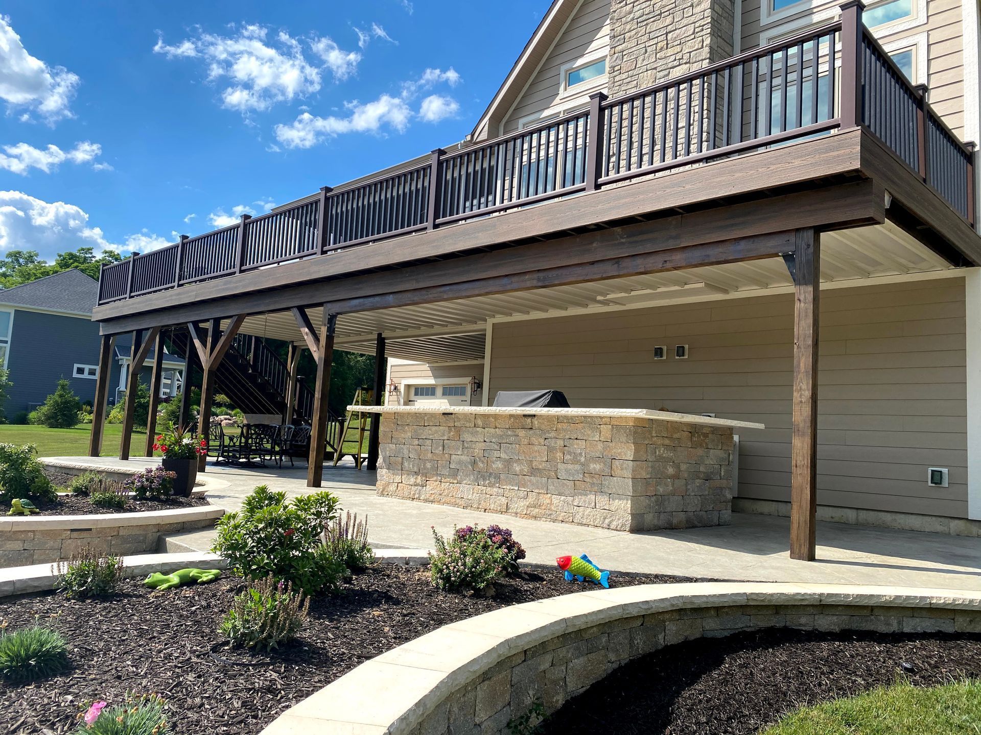 Covered patio and elevated deck on a house, with stone wall, stairs, and landscaped front yard.