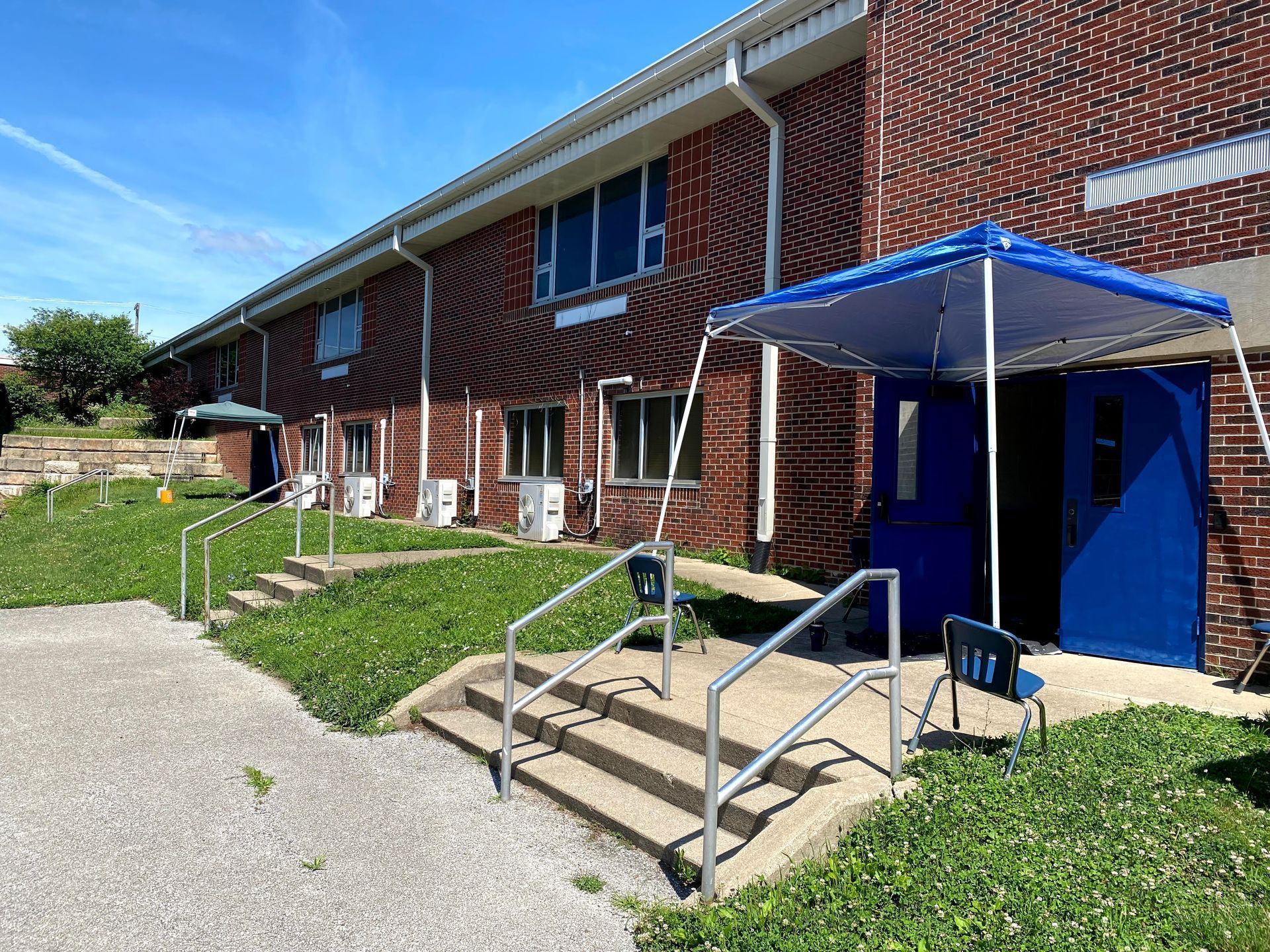 Brick apartment building entrance with blue accessibility ramp and canopy beside a sidewalk