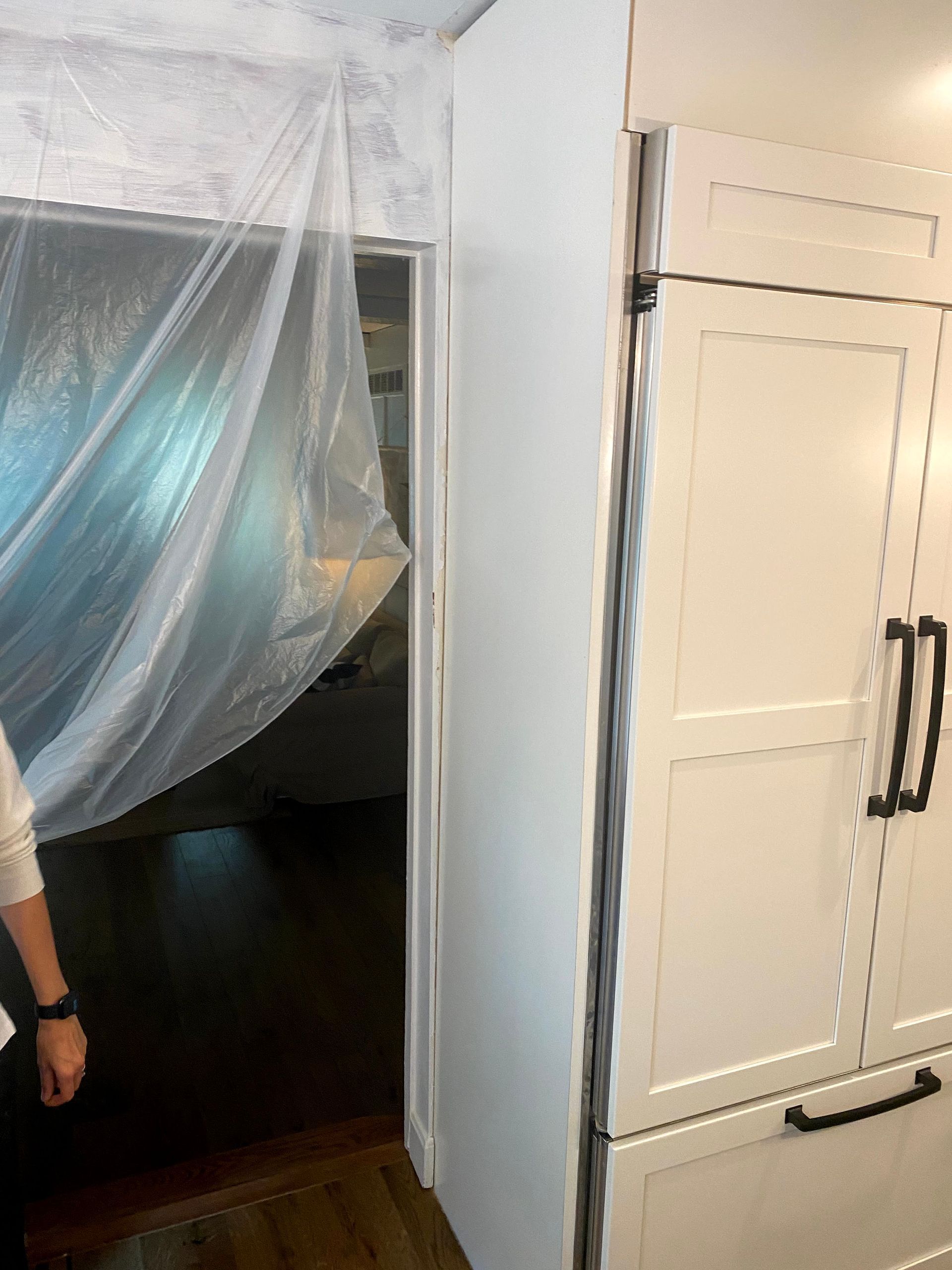 Plastic sheeting draped over a doorway beside a white cabinet with black handles