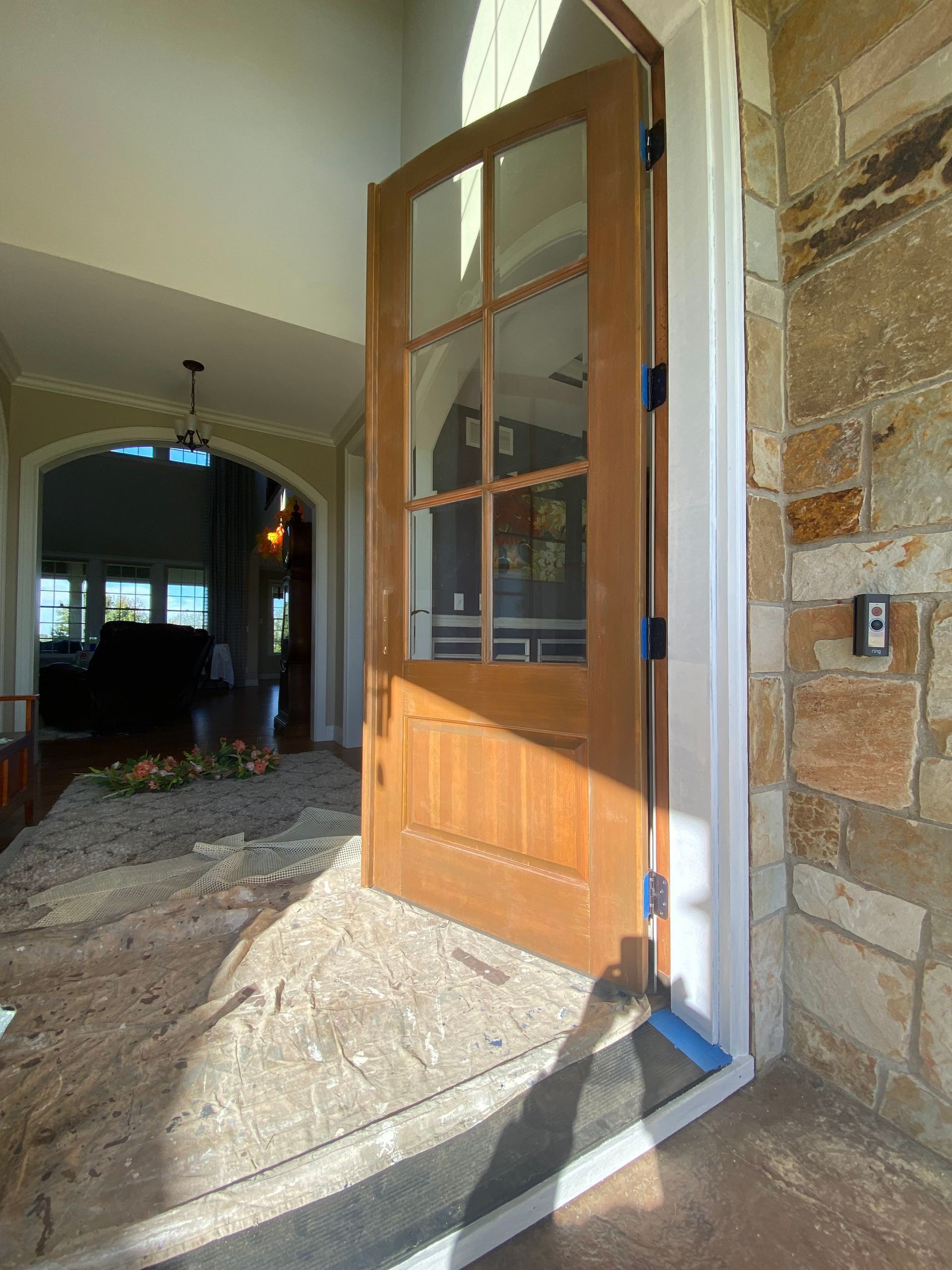 Open wooden front door in a stone entryway with sunlight streaming in.