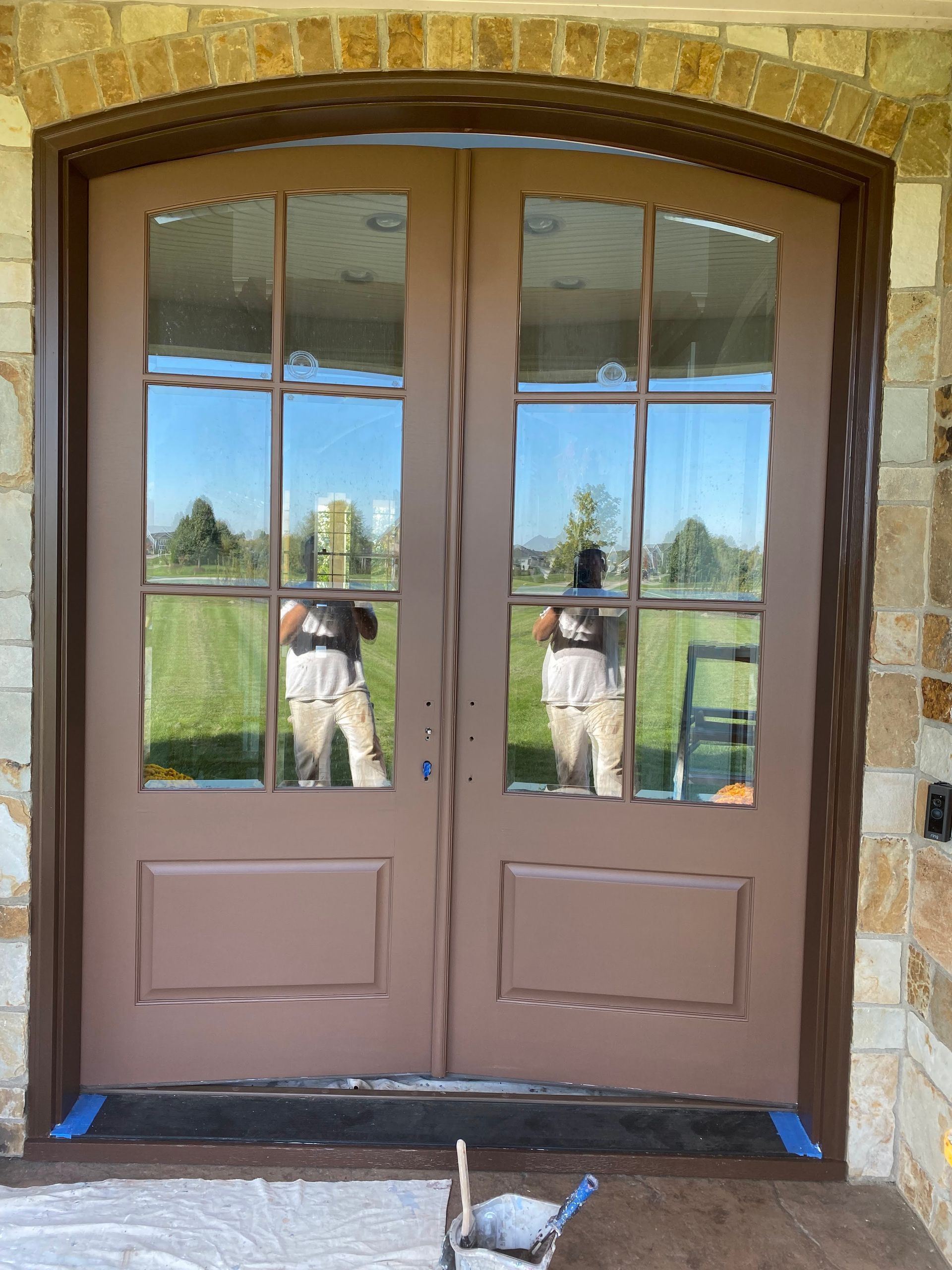 Brown double glass doors reflecting a person, set in a stone entryway with blue tape at the base