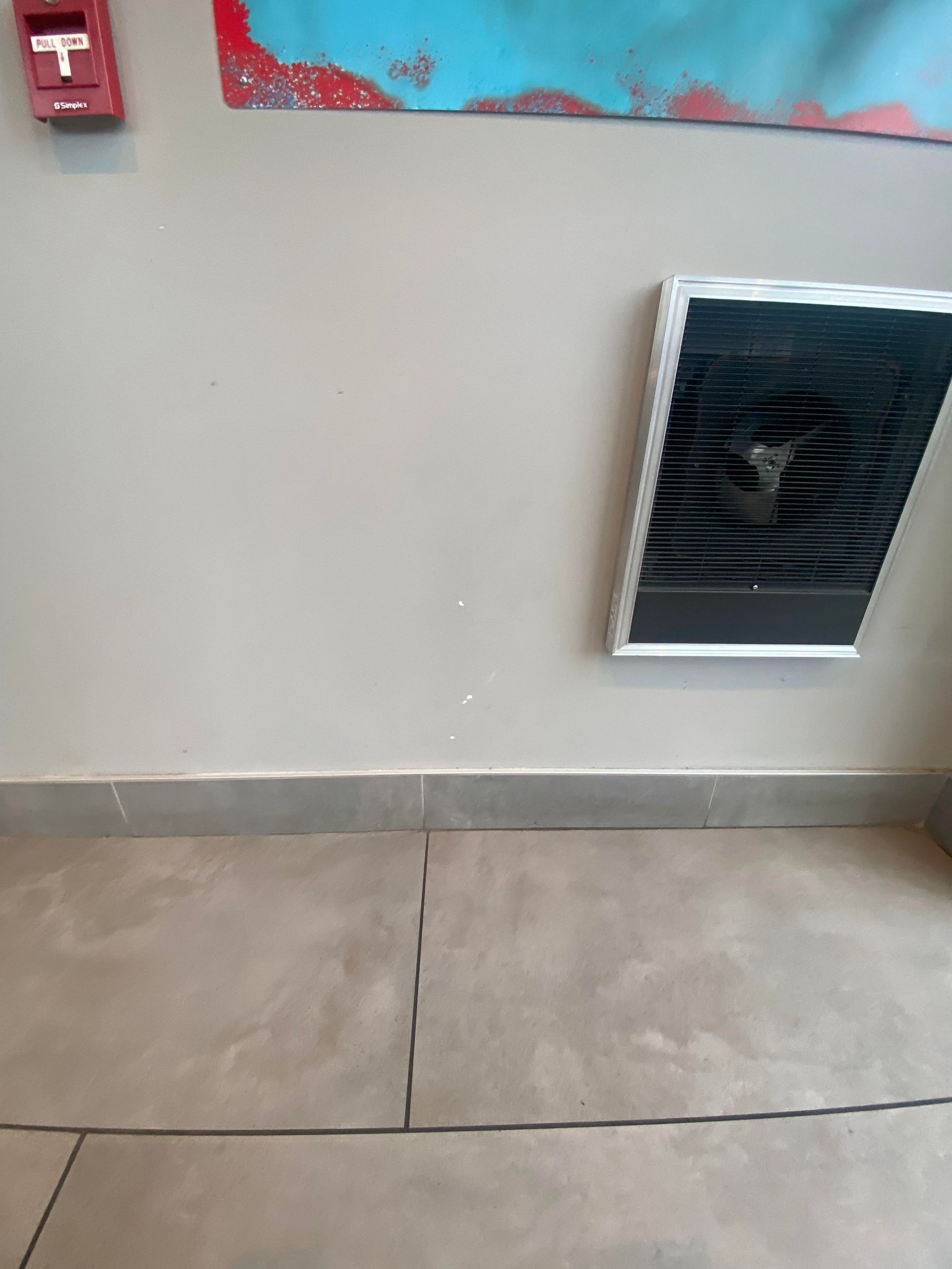 Indoor wall with a red fire alarm, a wall vent, and tiled floor