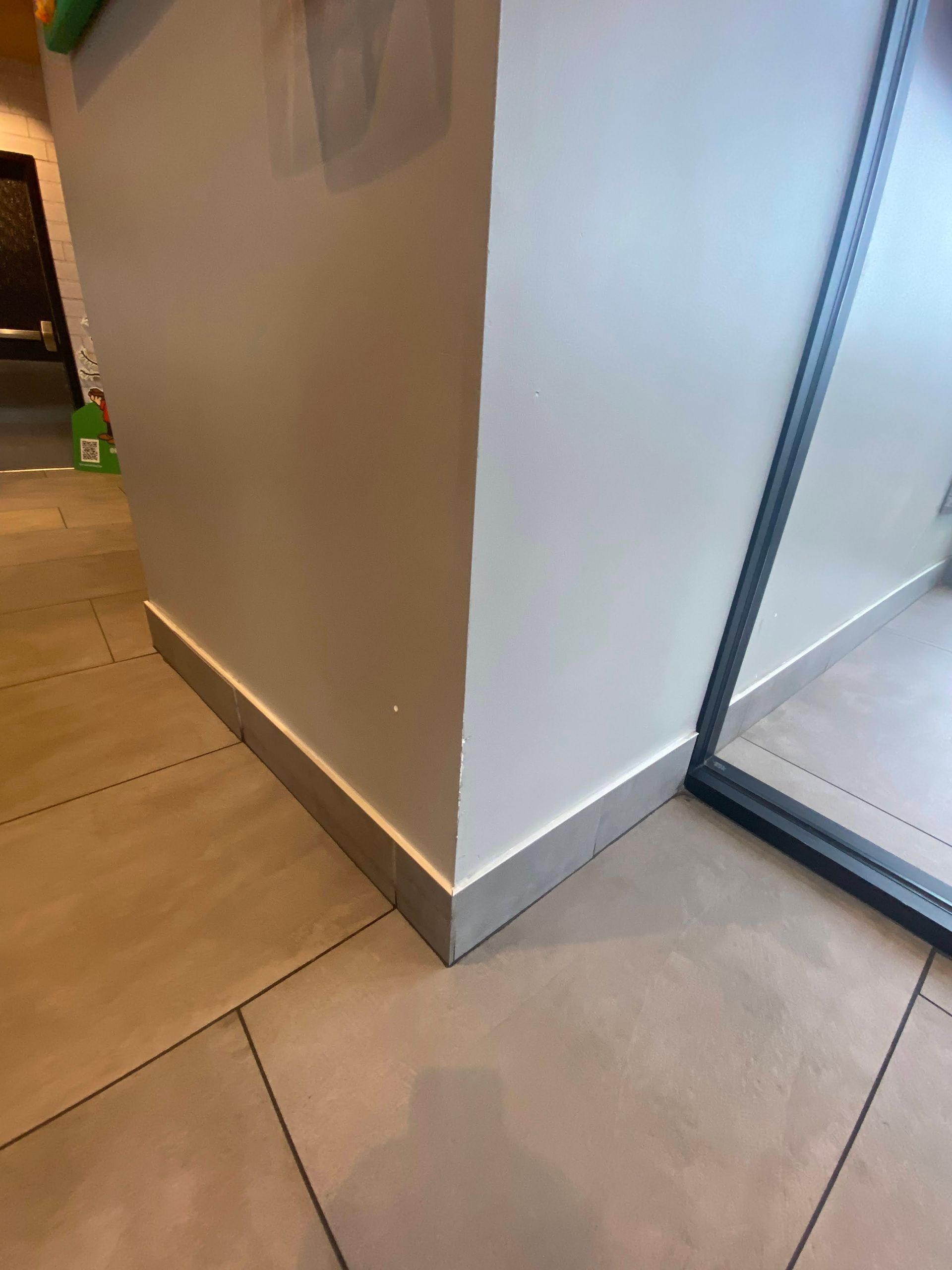 Corner of a beige wall with gray base trim beside a glass door on a tiled floor.