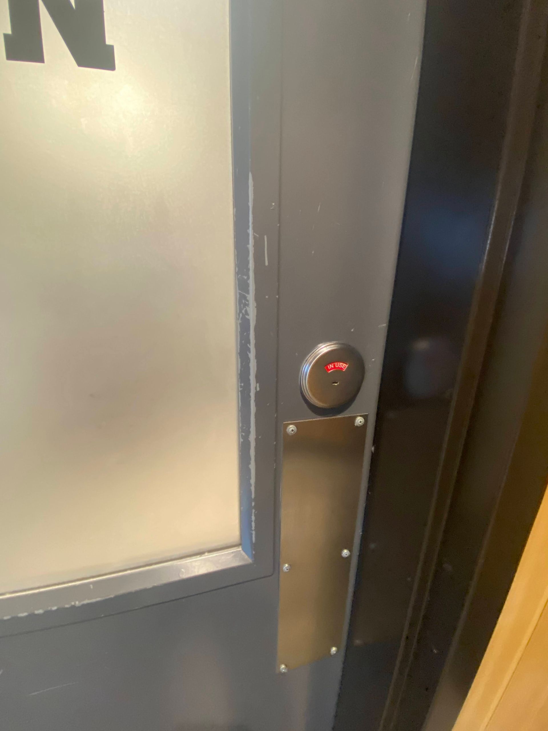 Close-up of an elevator call button and stainless steel panel beside a door.