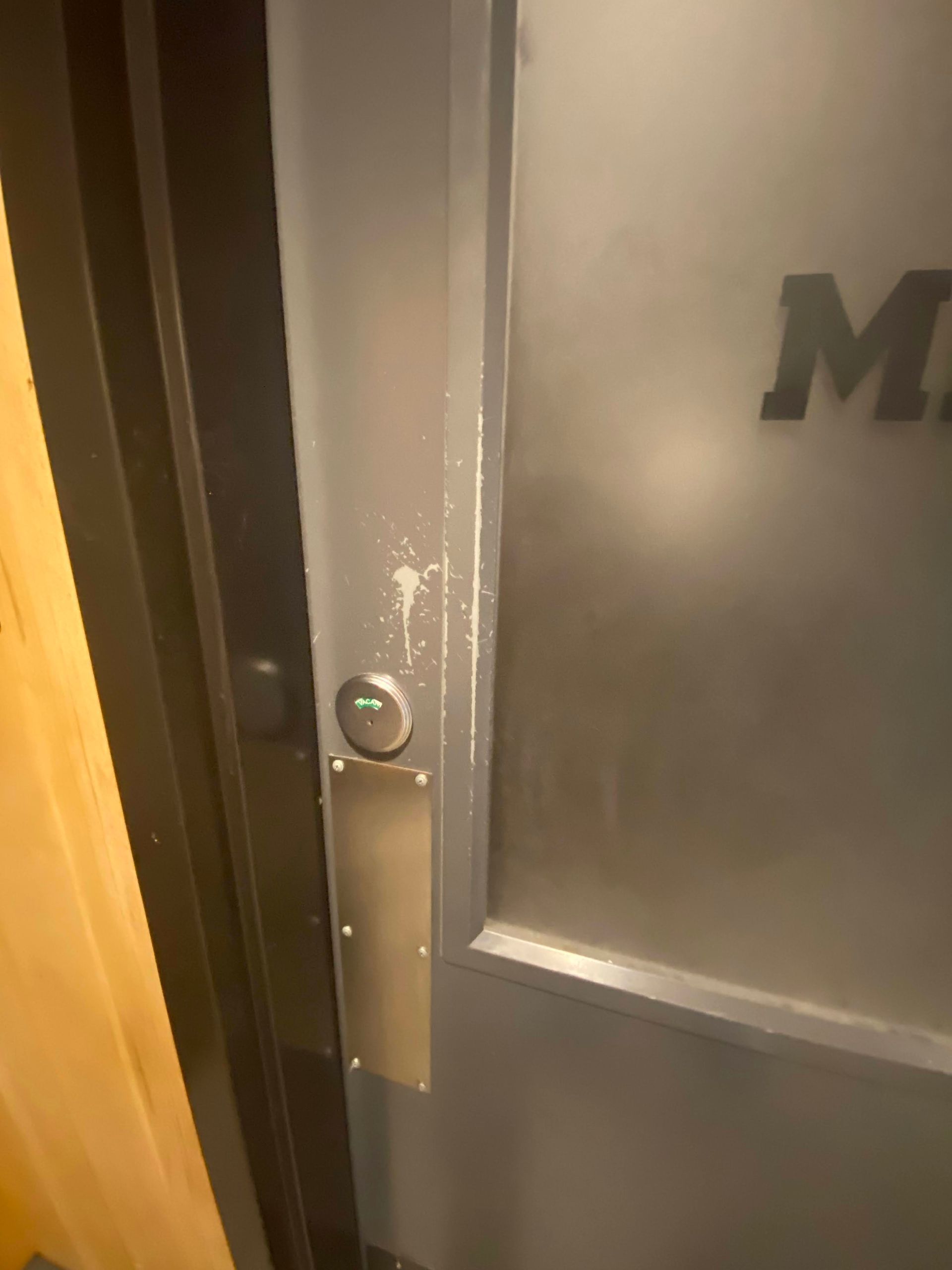 Close-up of a frosted metal door with a round lock and wood trim beside it