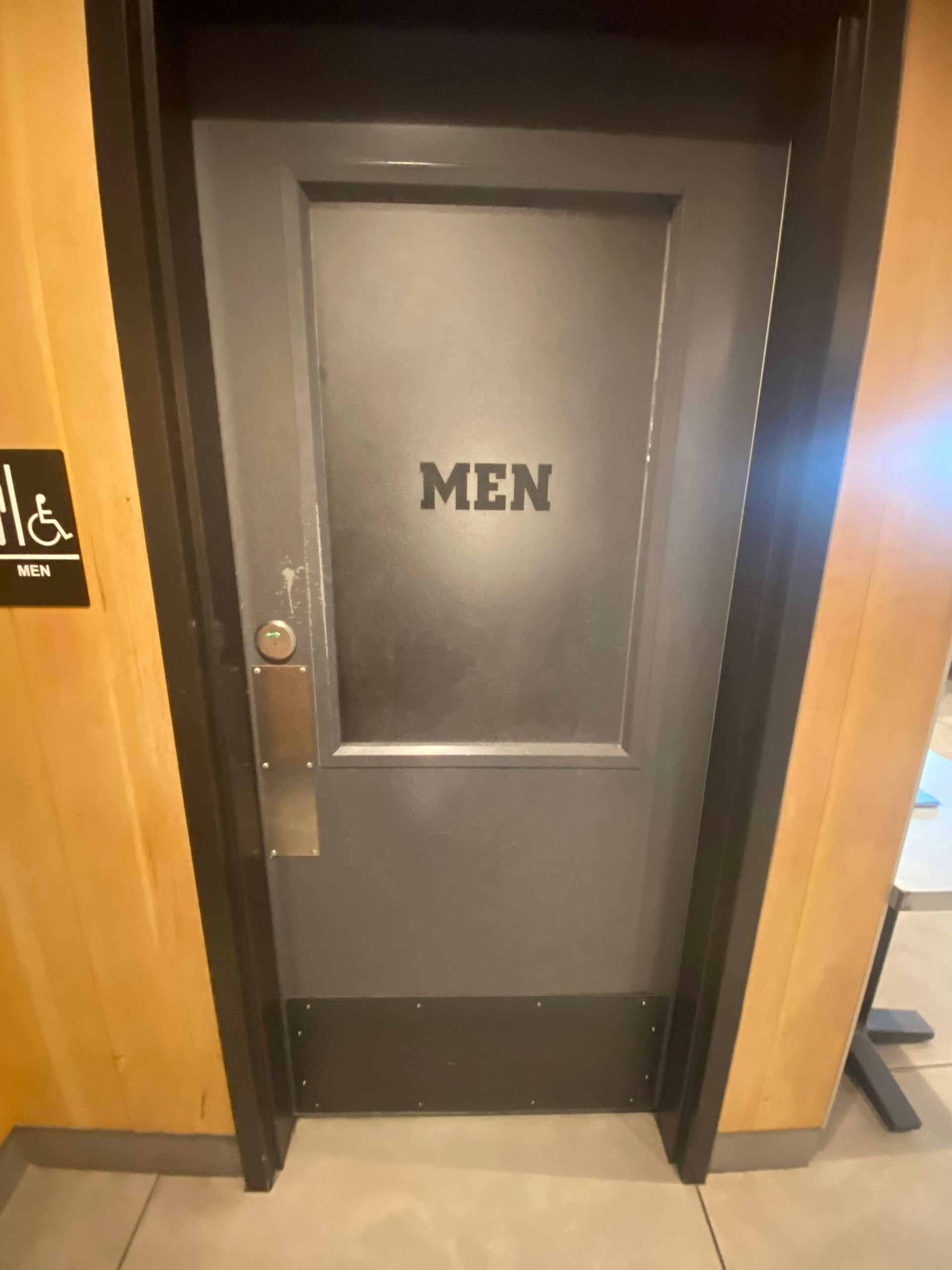 Closed dark gray men's restroom door with a black 