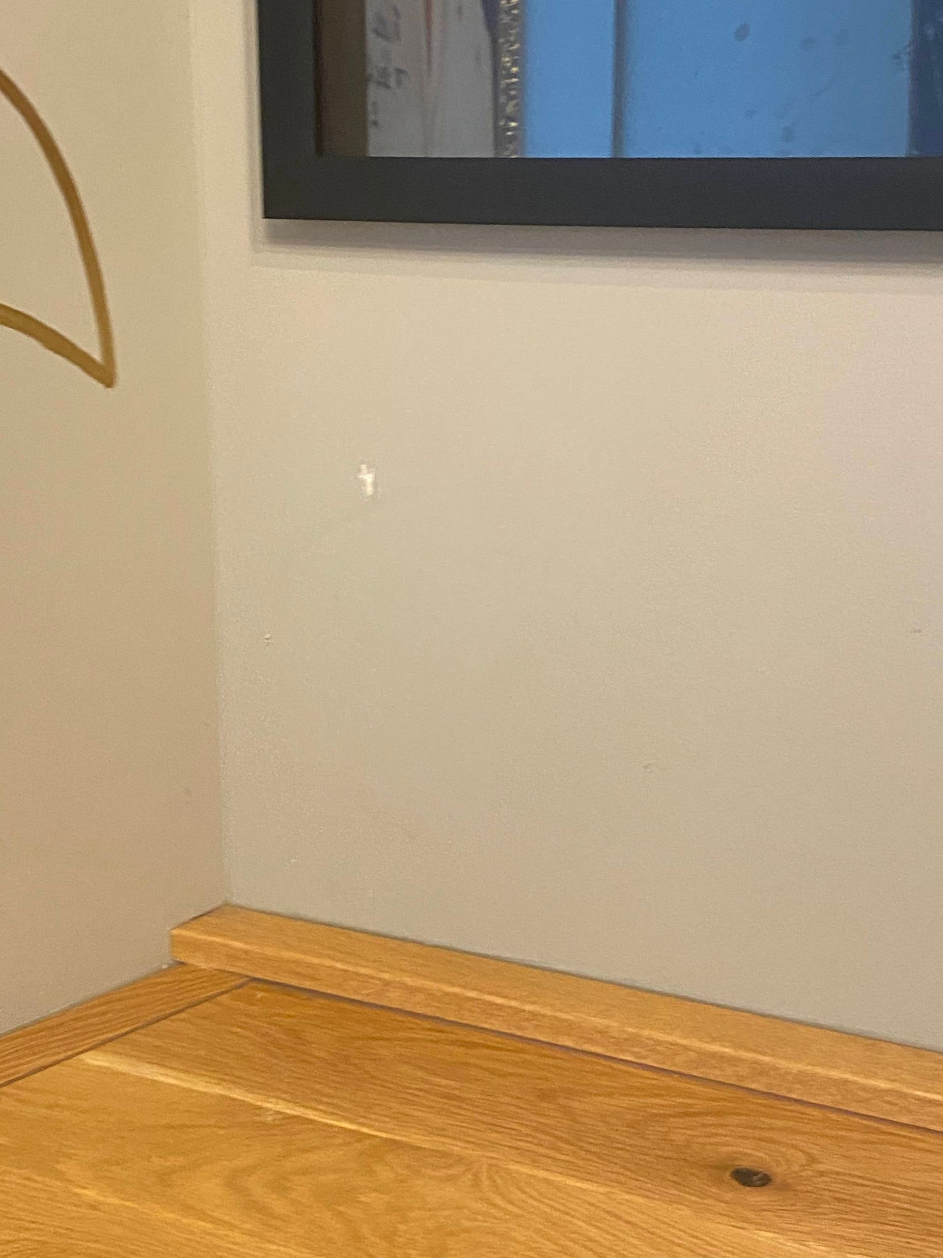 Empty corner with a wooden floor and a beige wall, with a framed picture partially visible above.