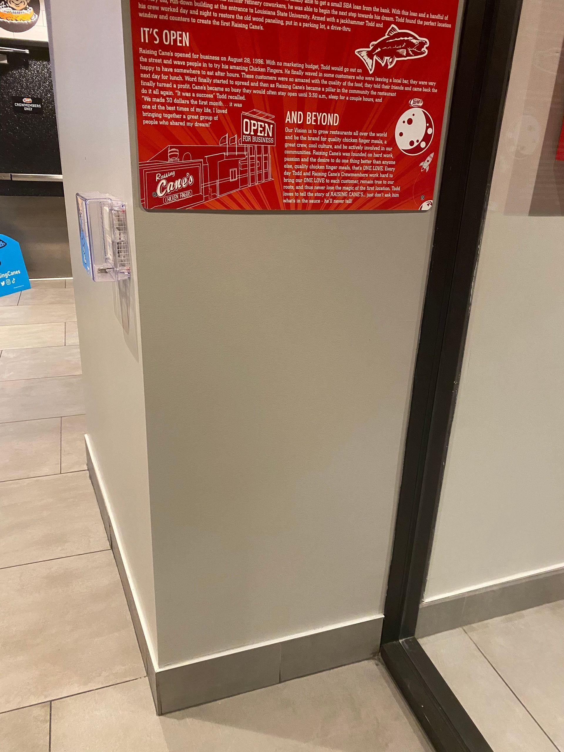 Red instruction sign on a beige wall beside a black-framed doorway in a tiled interior.