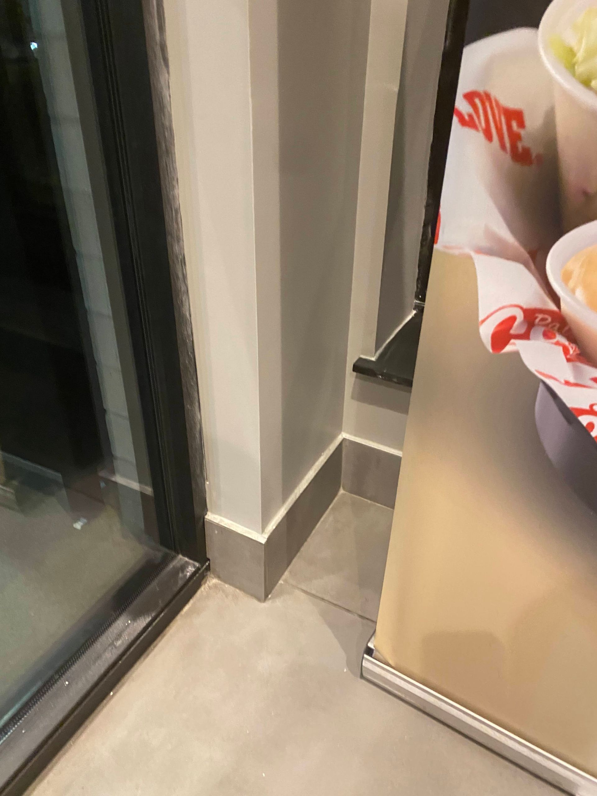 Corner of a room with a glass door, gray wall trim, and a poster showing food on the right.