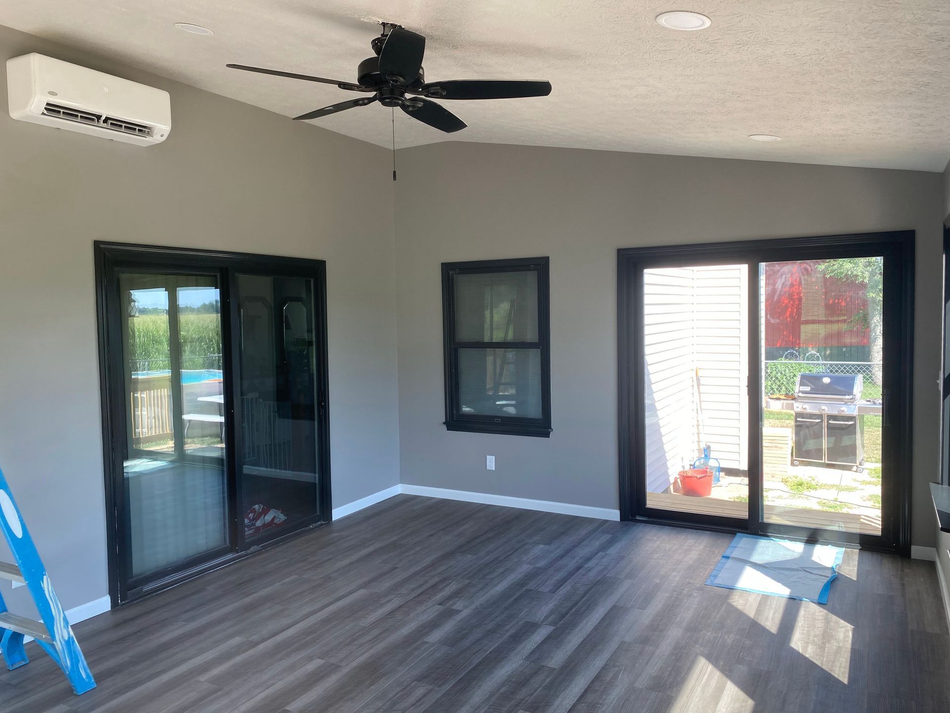 Empty screened-in patio with gray flooring, black ceiling fan, and sliding glass doors.
