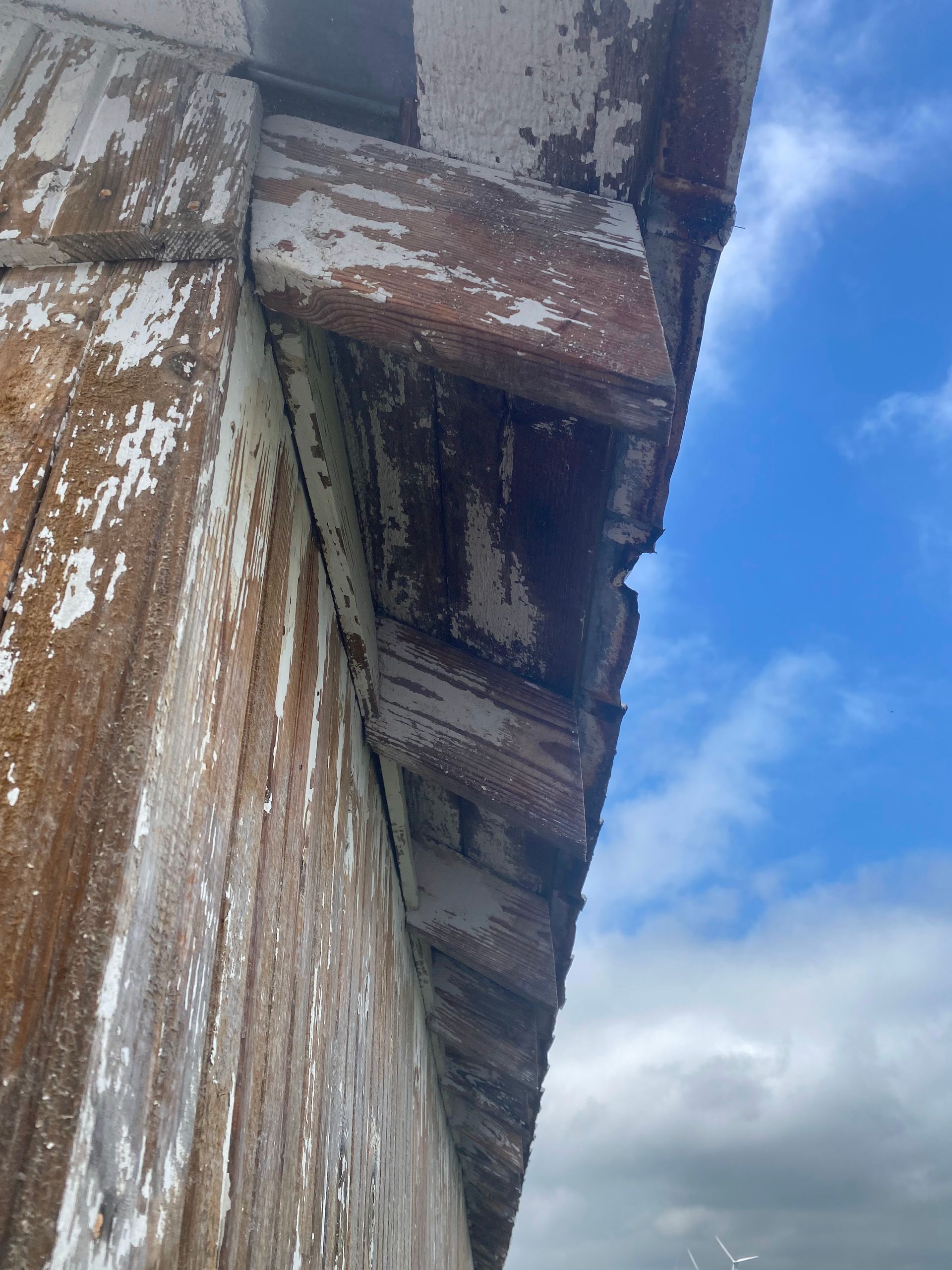 Close-up of a weathered wooden roof eave with peeling paint against a blue sky