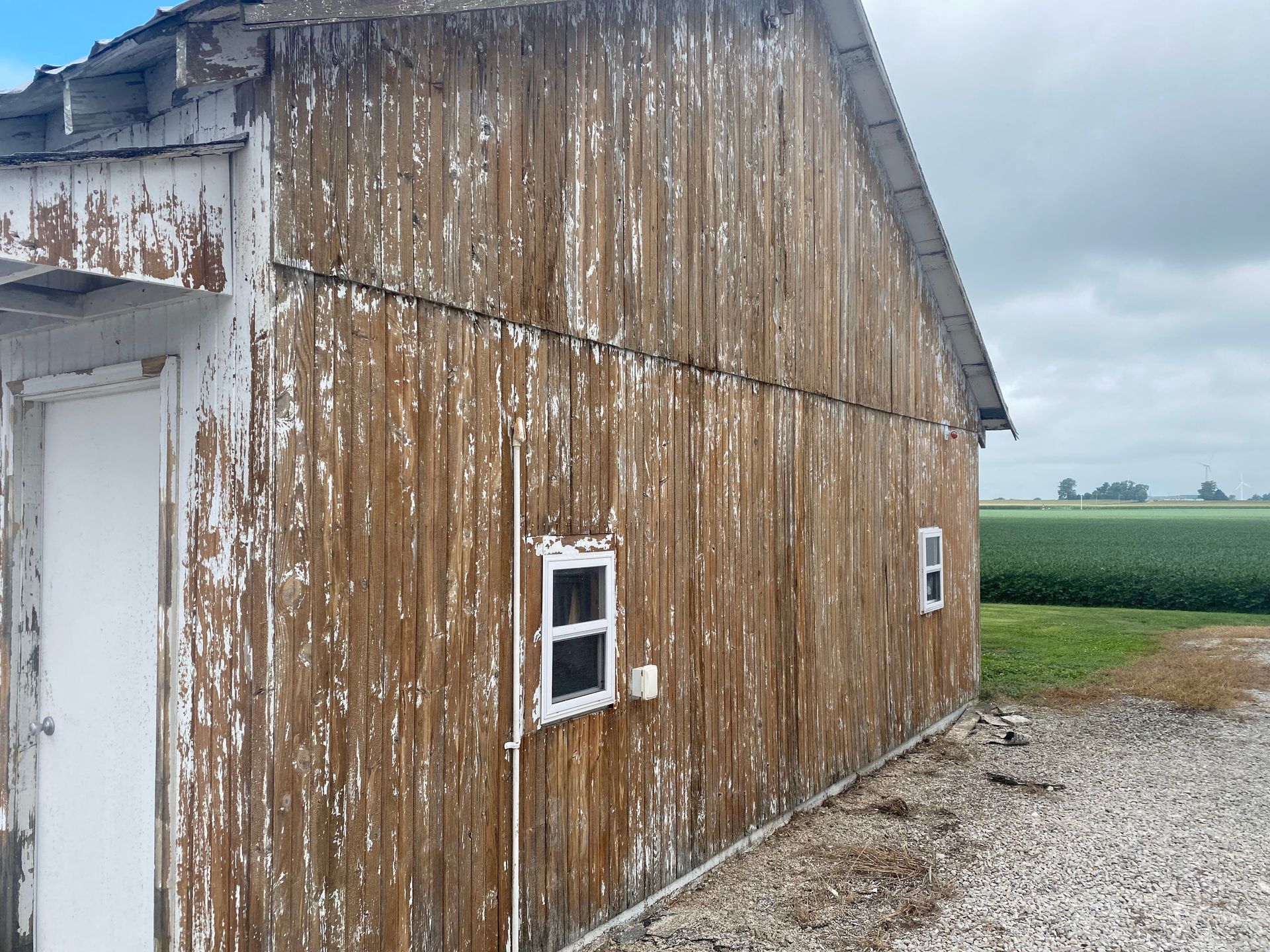Weathered wooden barn wall with peeling white paint beside a gravel lot and green fields.
