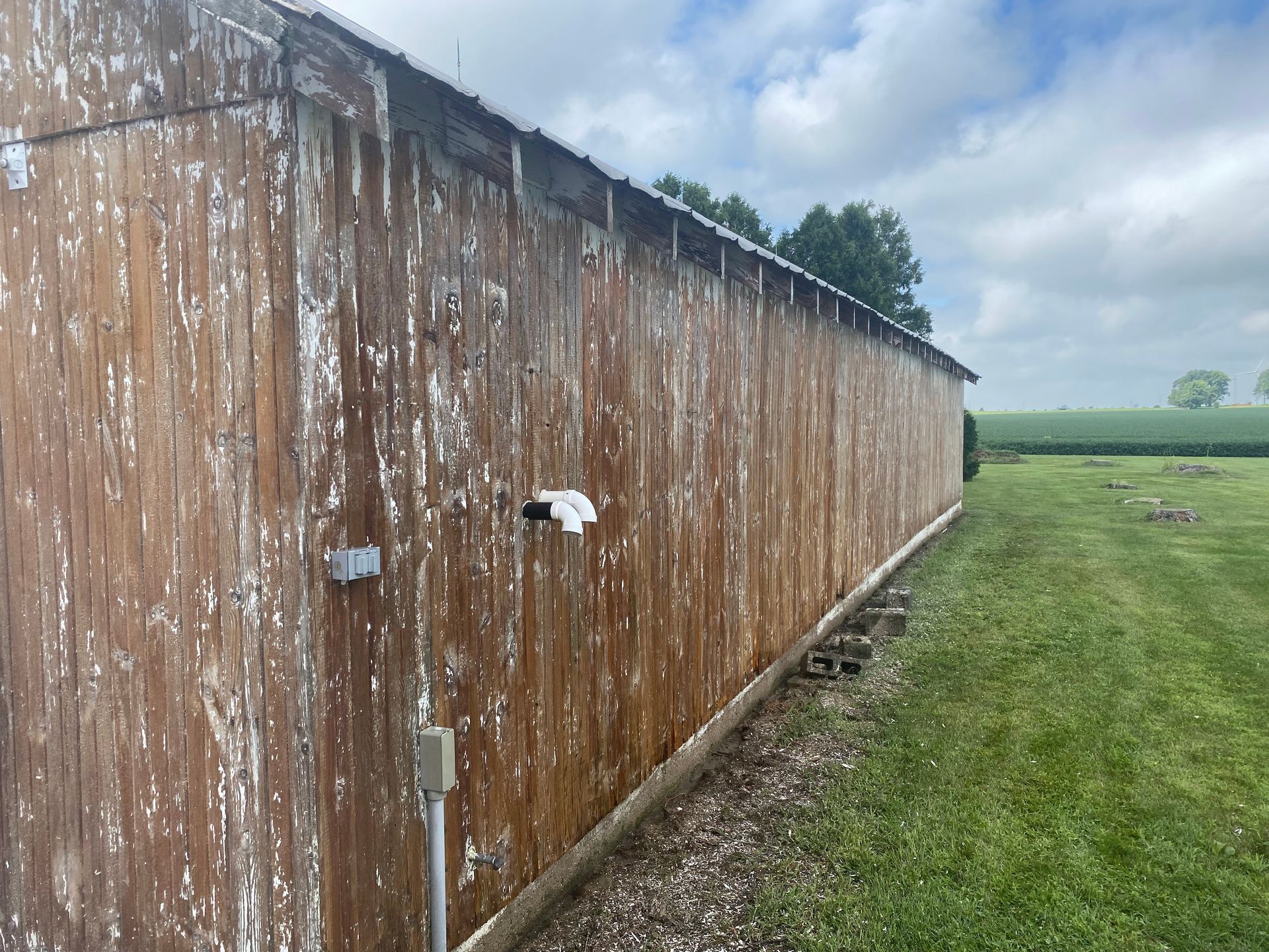 Rusty corrugated metal shed wall beside a grassy field under a cloudy sky