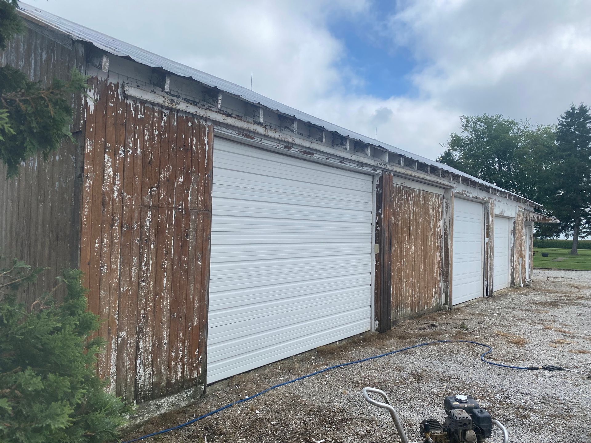 Row of weathered garage doors along a gravel driveway, one bright white door centered among rusted wood panels.