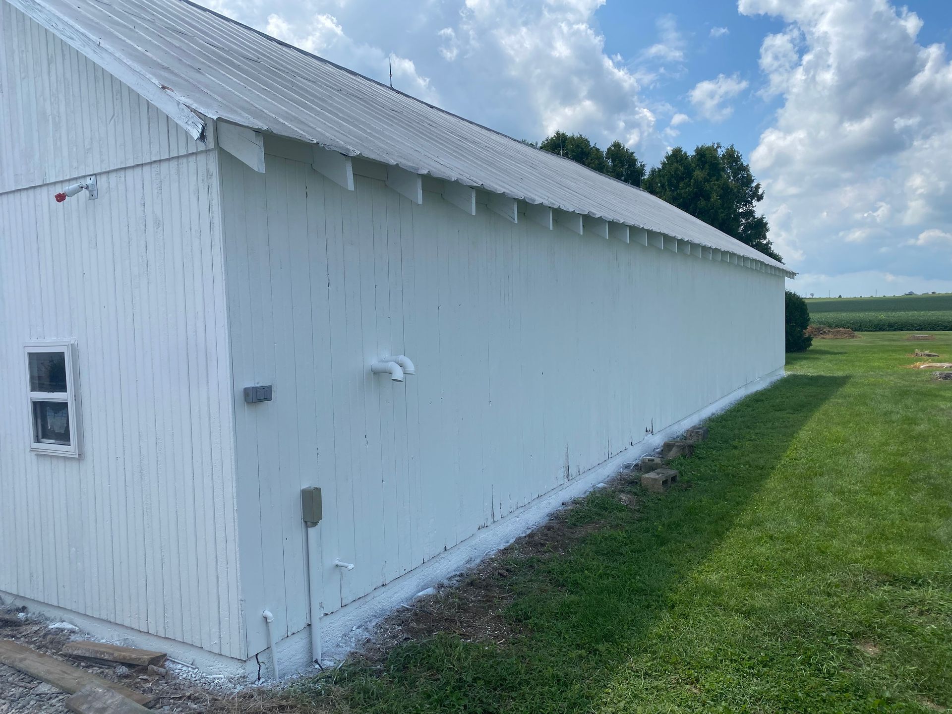 White barn with corrugated siding and a metal roof beside a grassy field under a blue sky.