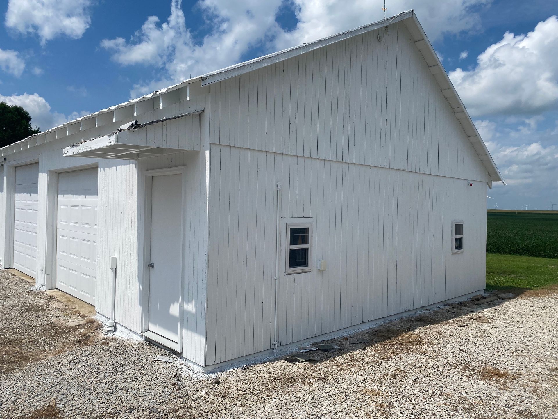 White barn or shed with double doors and small windows on a gravel lot under a cloudy sky