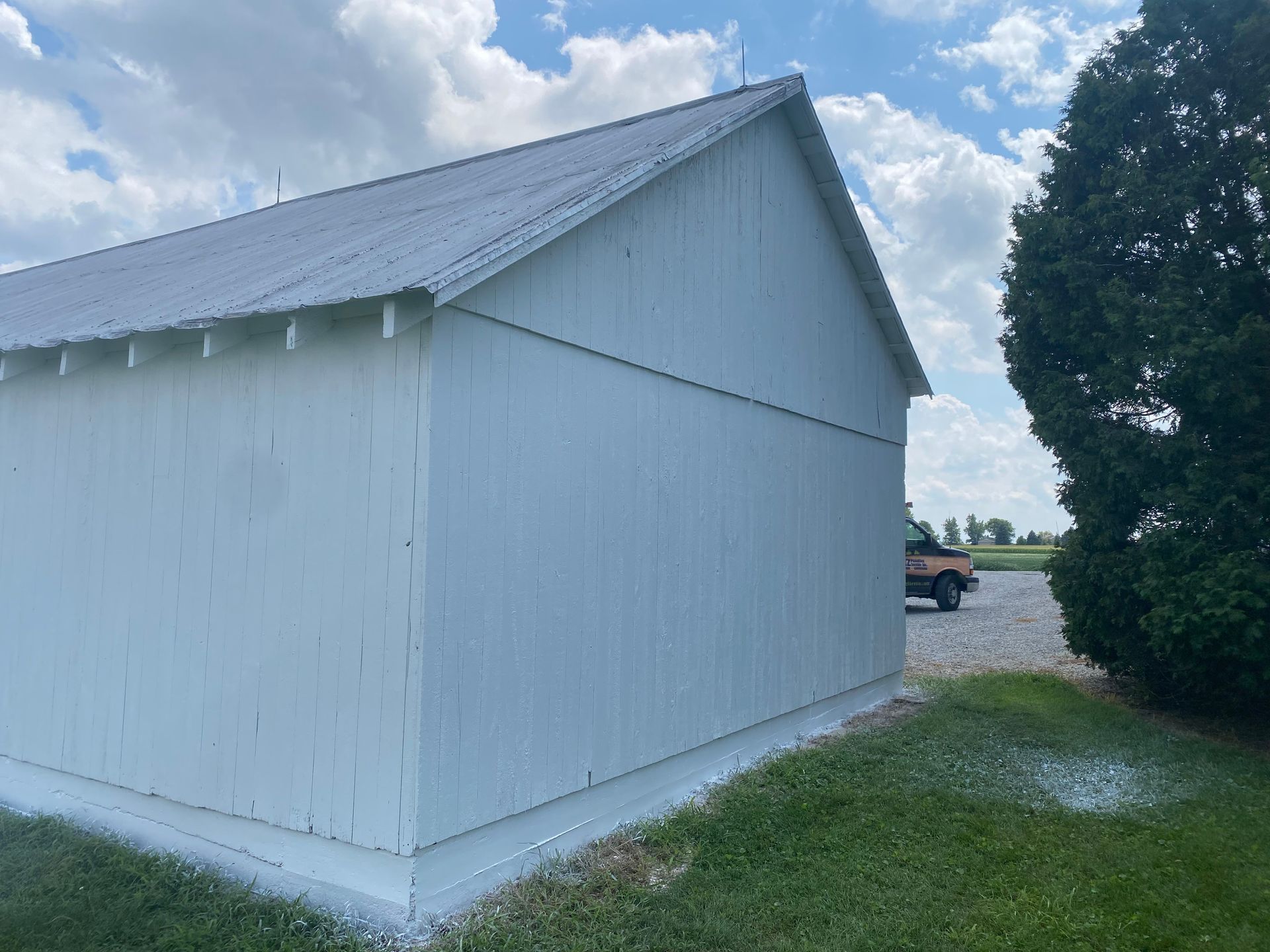 White barn-like building with a metal roof beside a grassy path under a cloudy sky