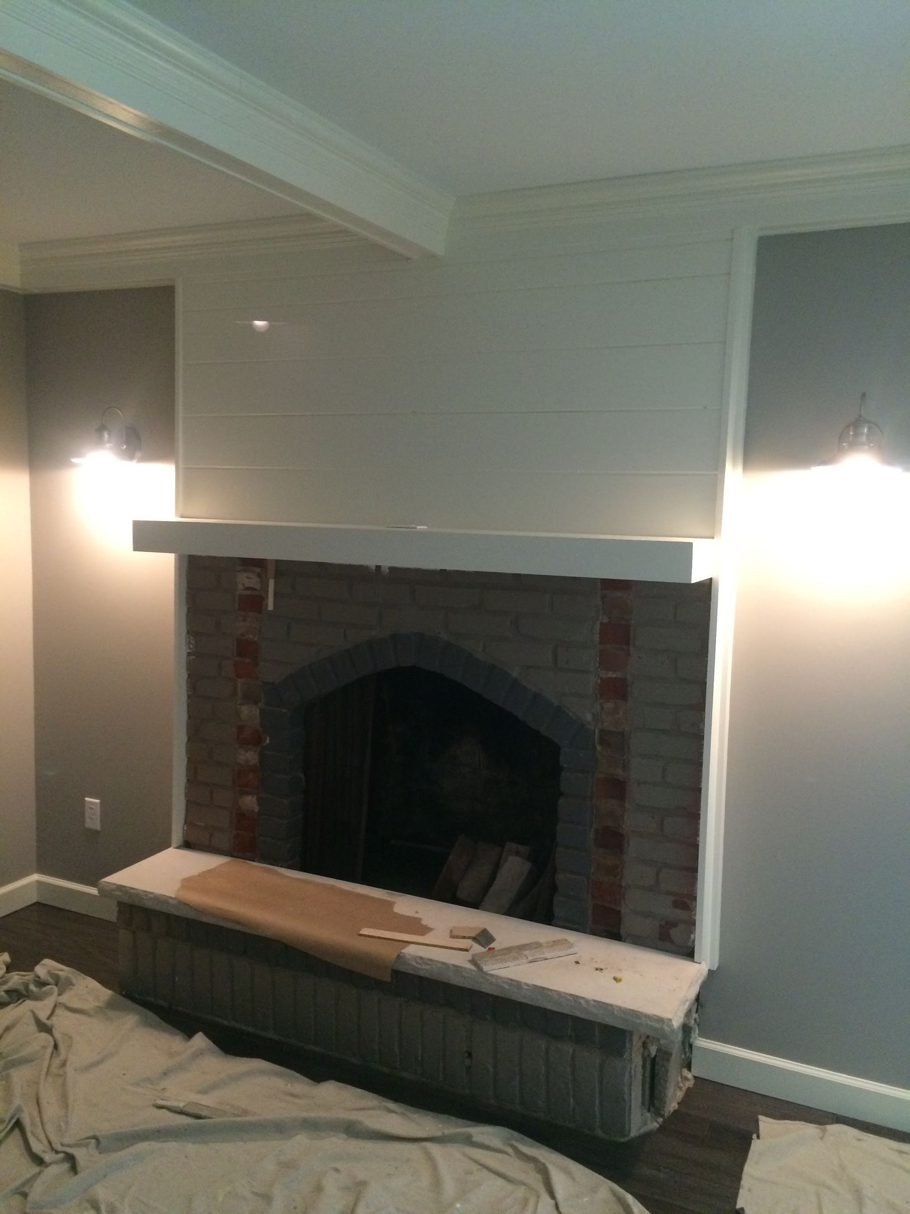 Living room with brick fireplace, white mantel, wall sconces, and a radiator in front