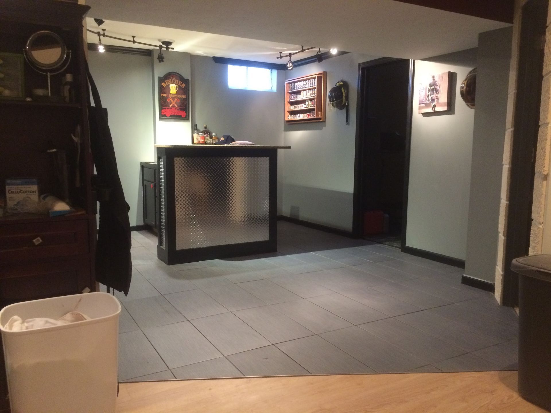 Empty indoor lounge with gray floor tiles, a bar counter, wall decor, and a trash bin in the foreground