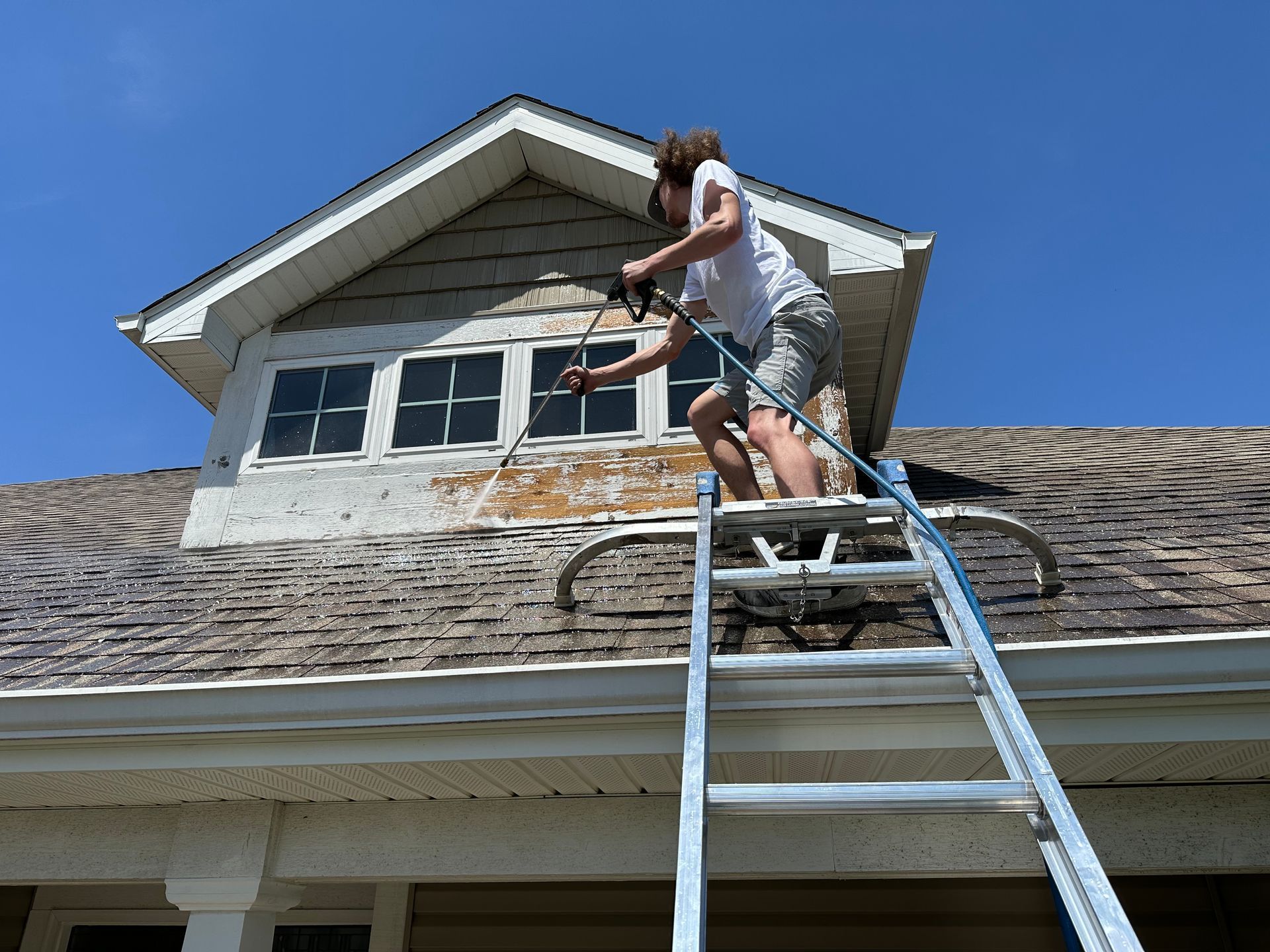 Person on a ladder repairing a roof dormer under a clear blue sky