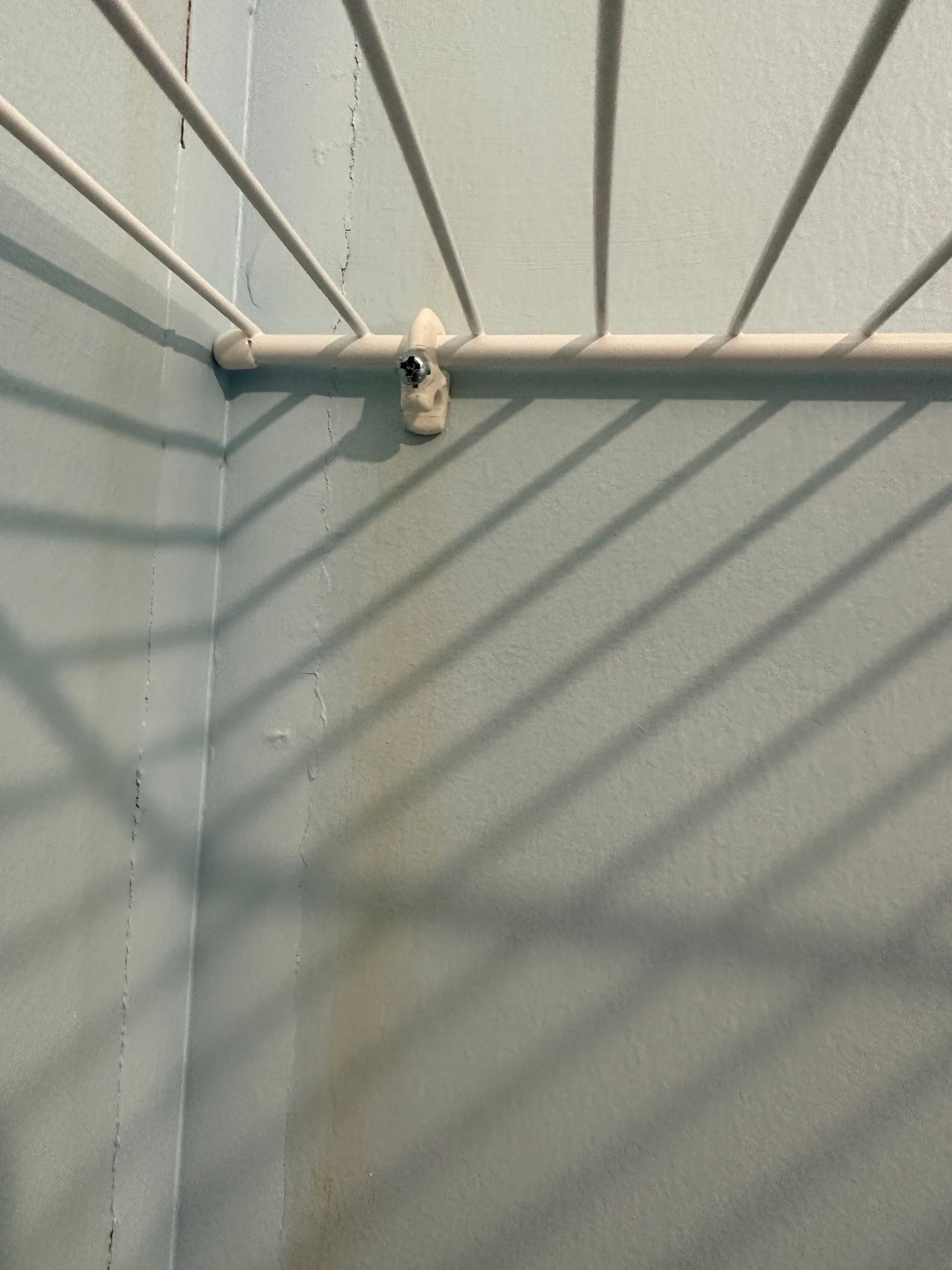 Empty light blue corner with a white pipe and a small hanging object on the wall.