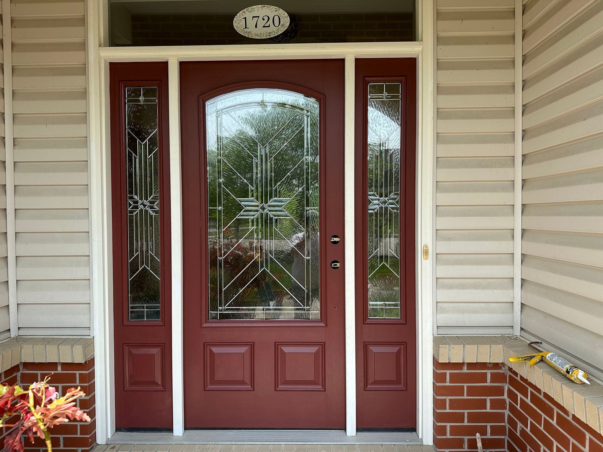 Front porch with a red front door, sidelights, and decorative glass panels, set in beige siding and brick.