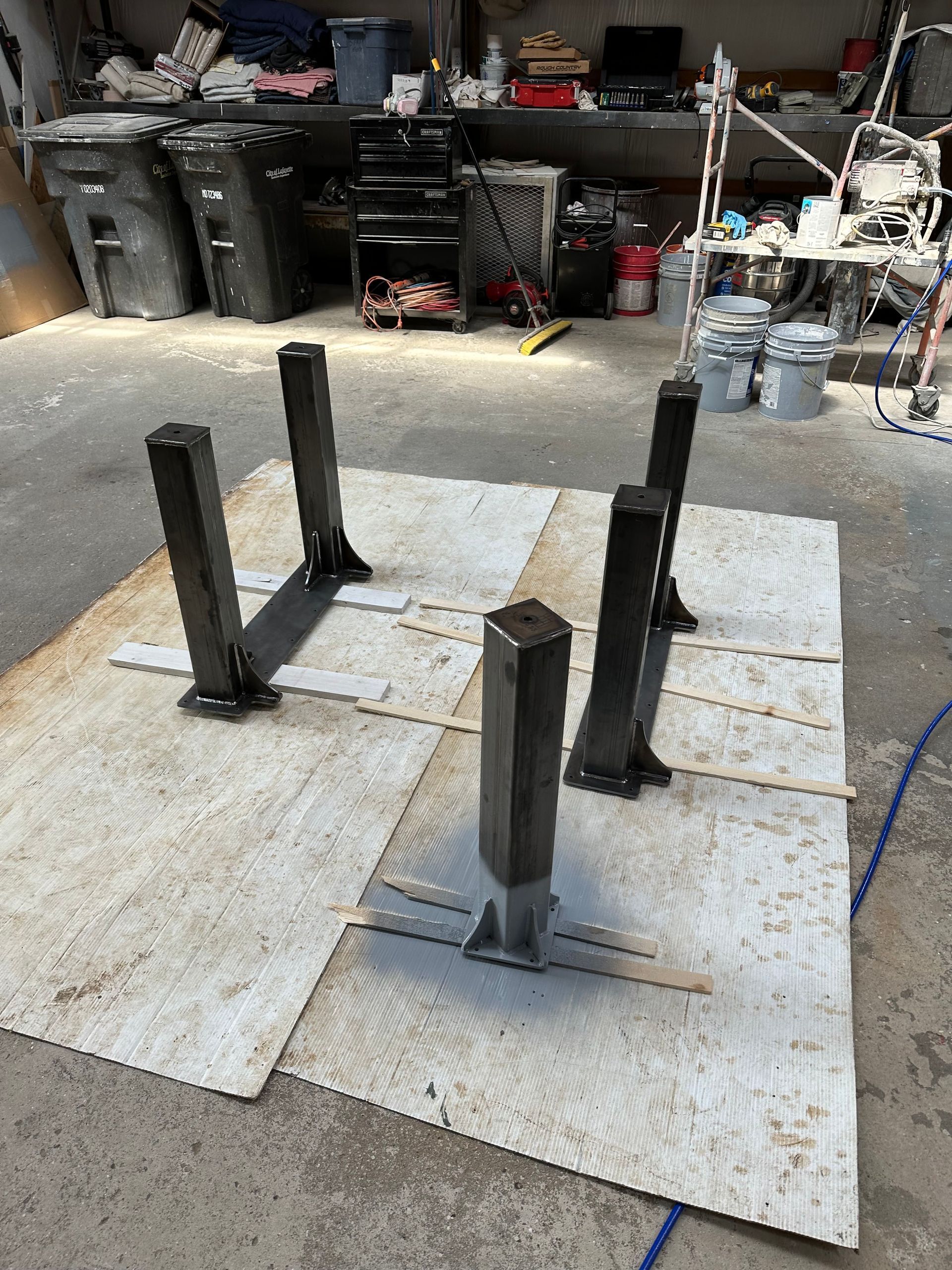 Four black metal posts mounted on white boards in a workshop or garage.