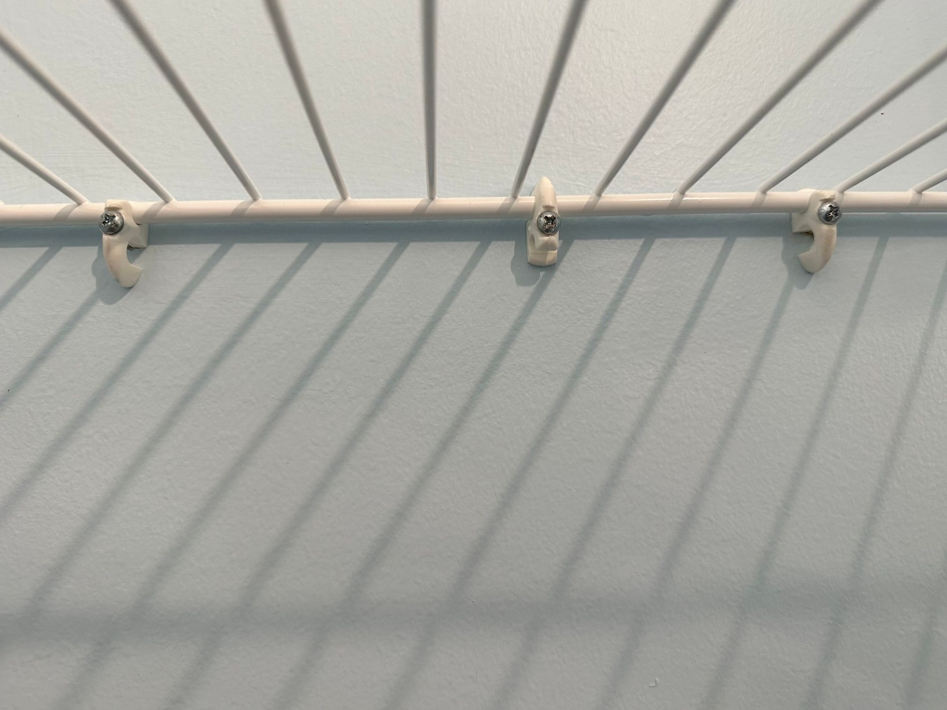 Three silver hooks mounted on a white slatted wall above a gray panel.