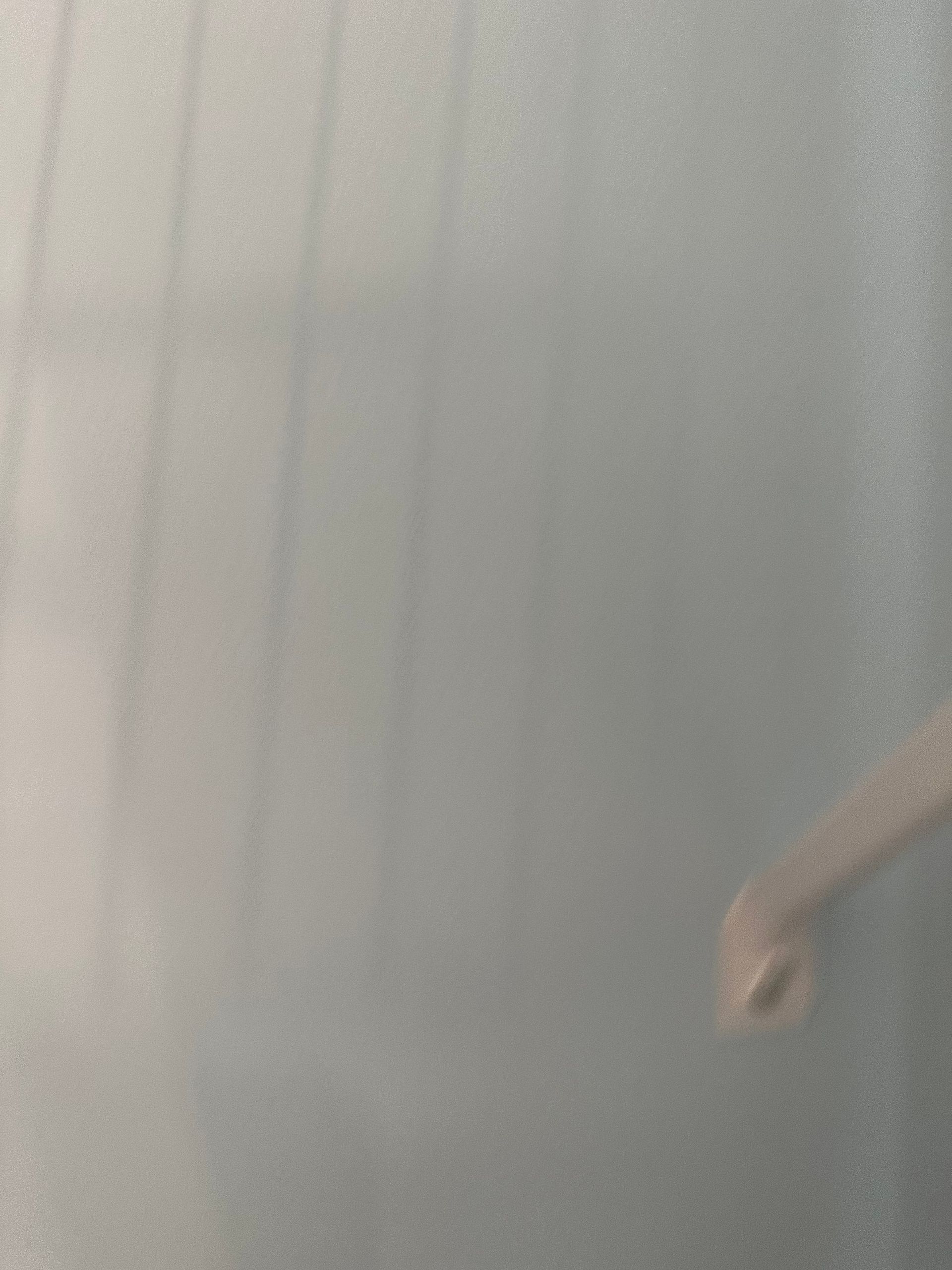 A person’s arm and hand beside a light gray curtain in soft indoor lighting