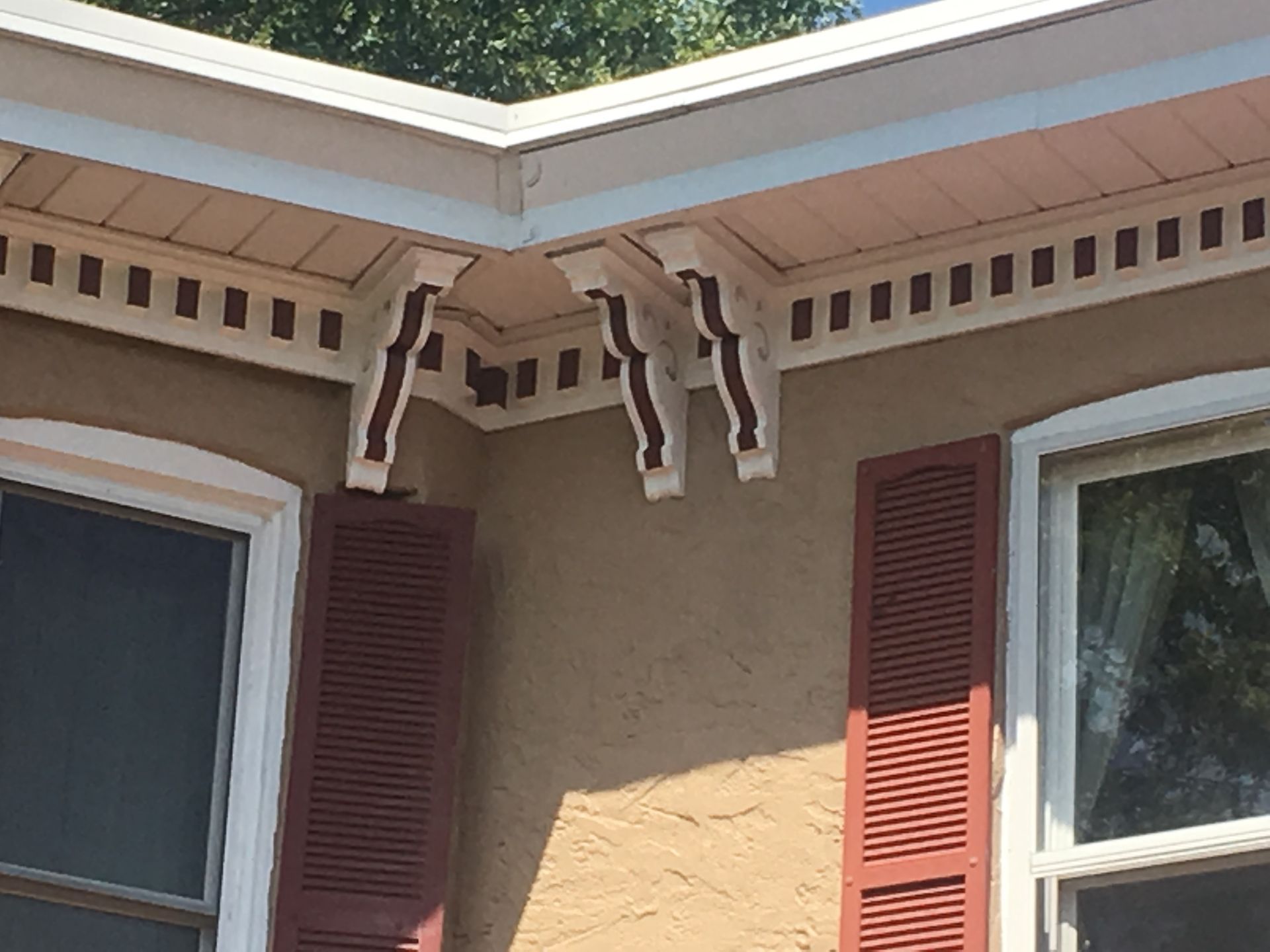House eaves with decorative brackets above tan siding and red shutters