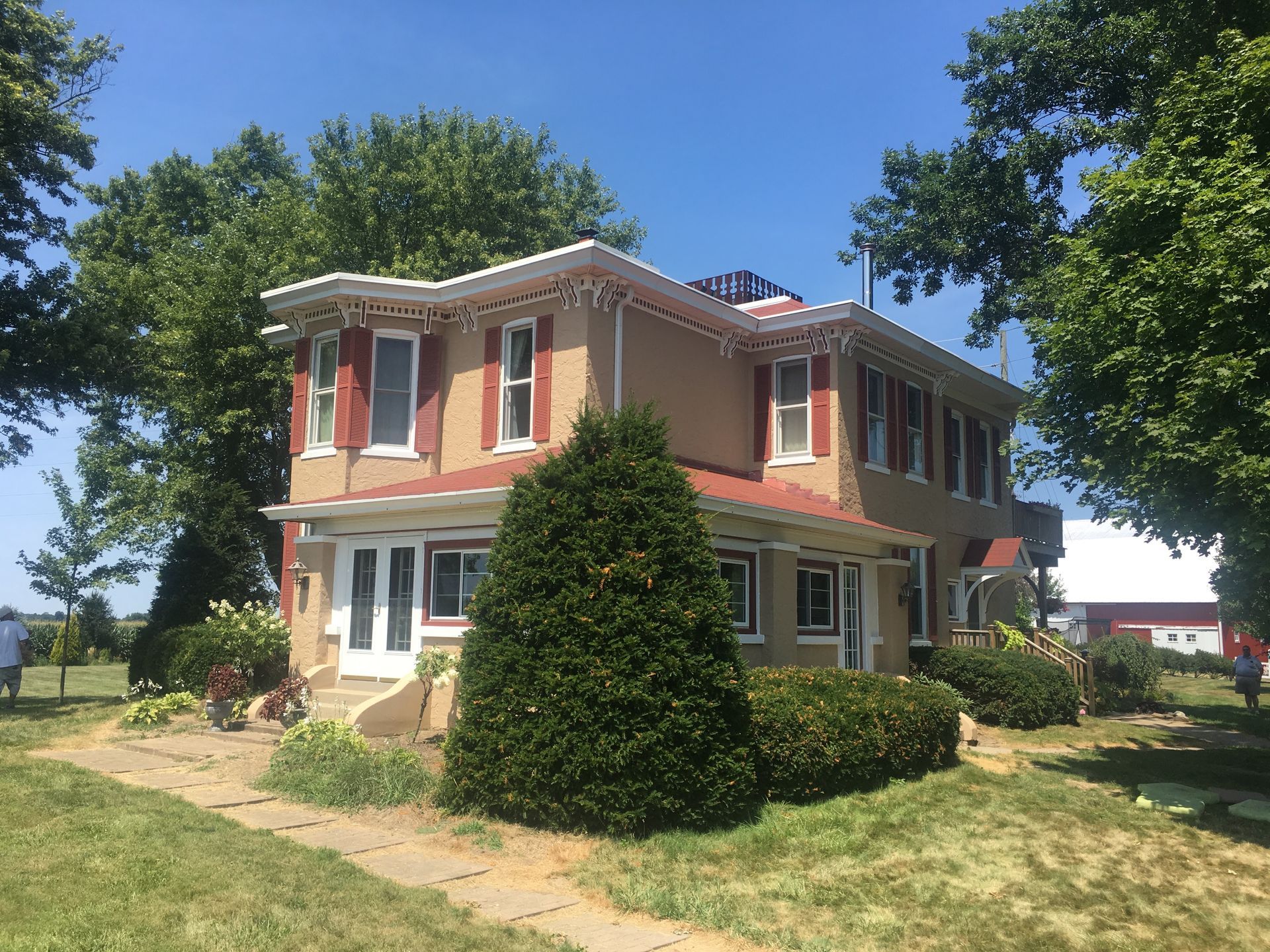 Two-story peach house with white trim and a large evergreen shrub in front on a sunny day